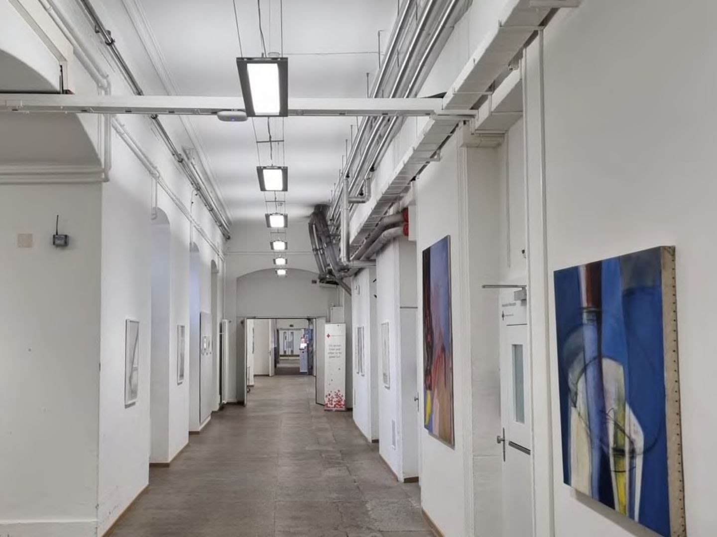 Long couloir lumineux avec œuvres d’art, murs blancs et un éclairage LED.