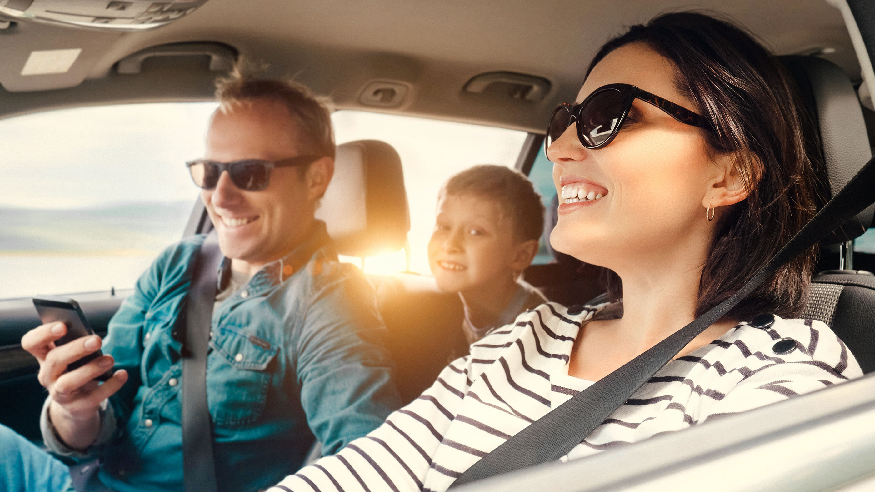 Une femme, un homme et un garçon conduisent une voiture à travers un paysage au coucher du soleil.
