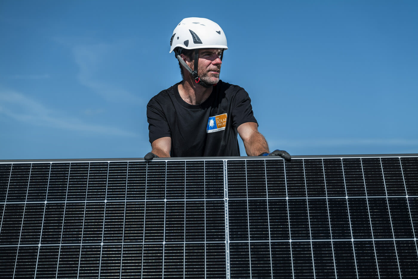 Une personne portant un casque de sécurité tient un panneau solaire sous un ciel bleu.