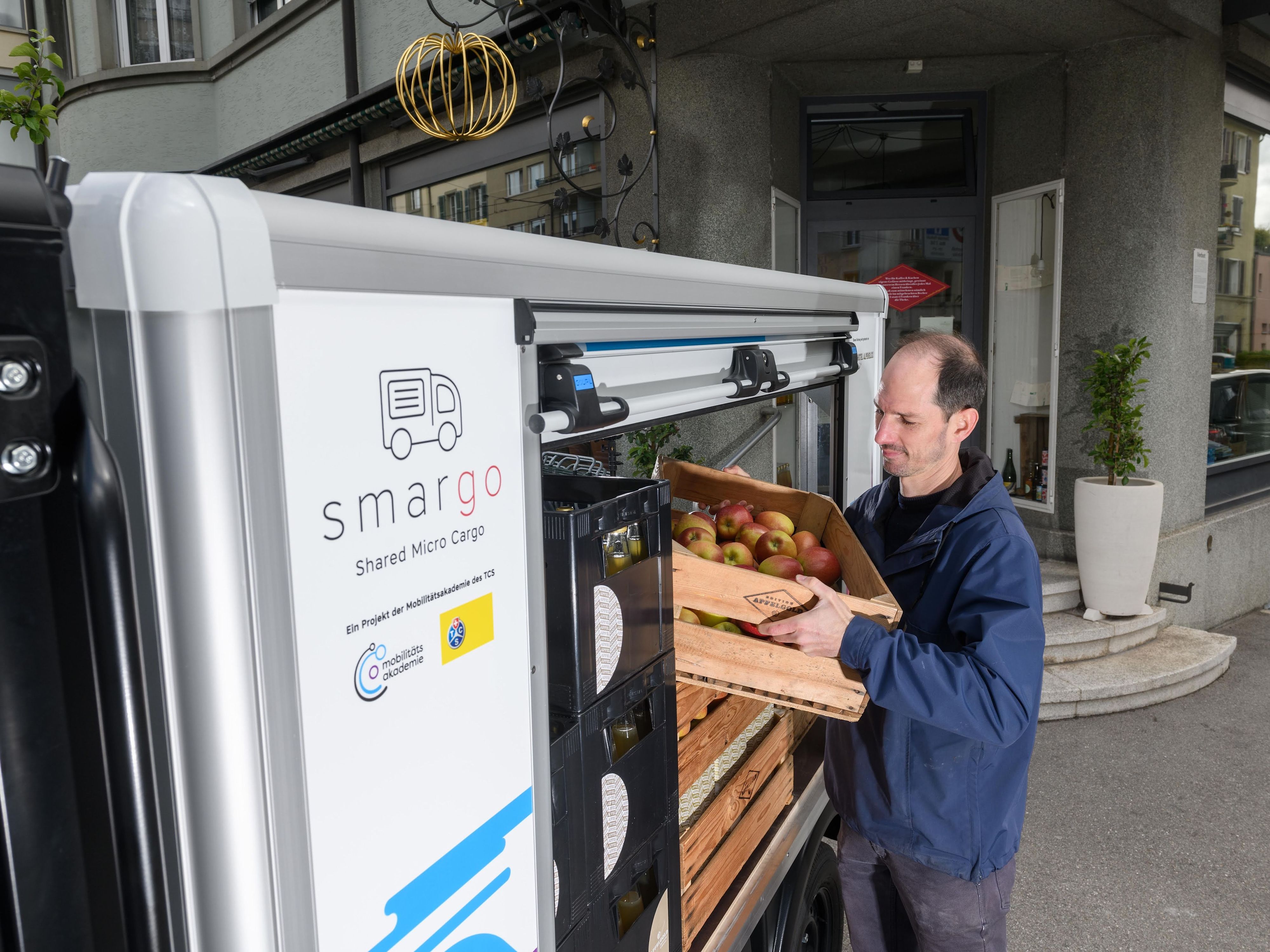 Un homme charge une caisse de pommes dans une camionnette électrique partagée.