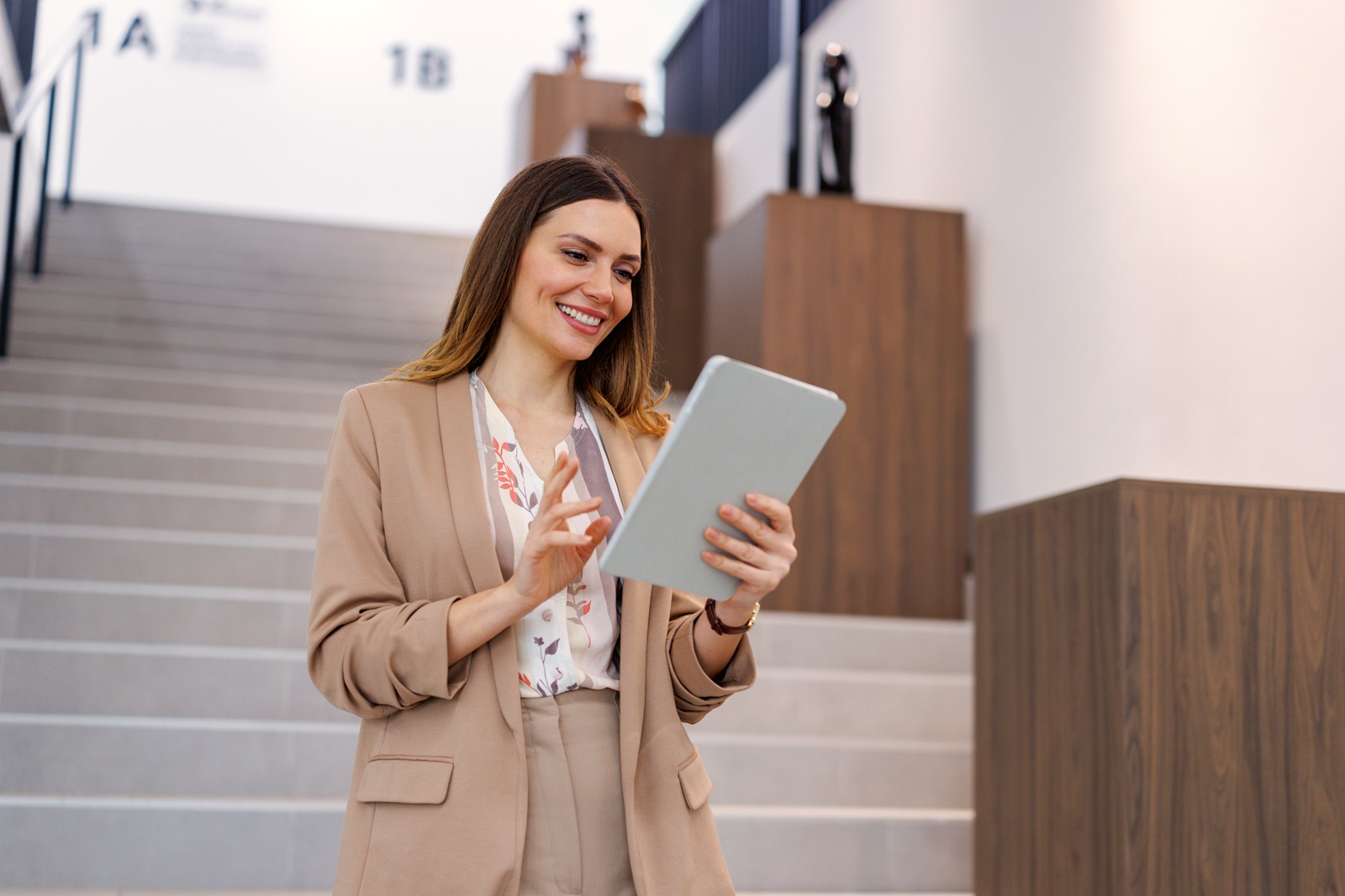 Donna in abbigliamento professionale che utilizza un tablet in un ambiente moderno con una scala sullo sfondo.