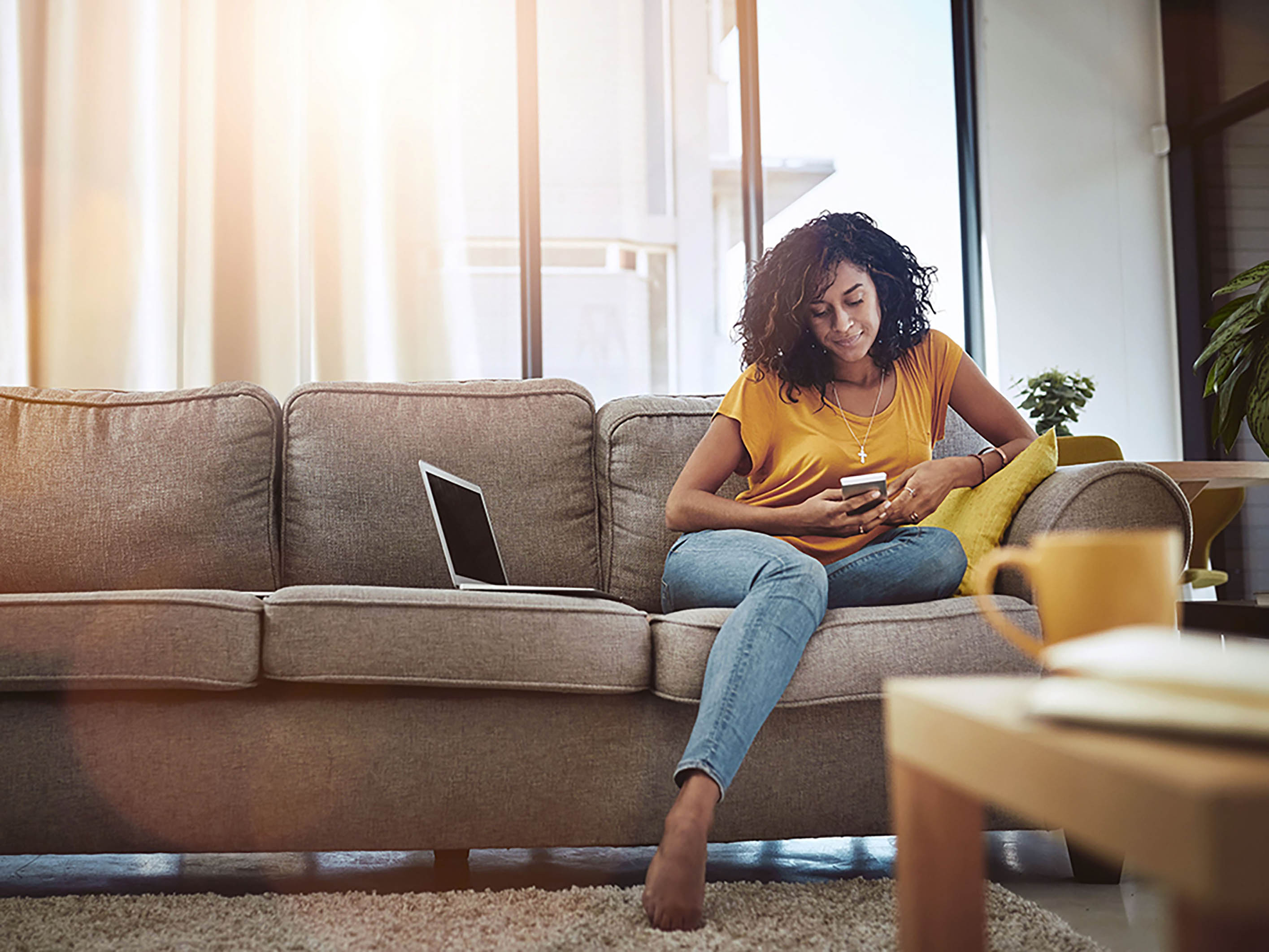 Une femme est assise sur un canapé et regarde son téléphone portable.