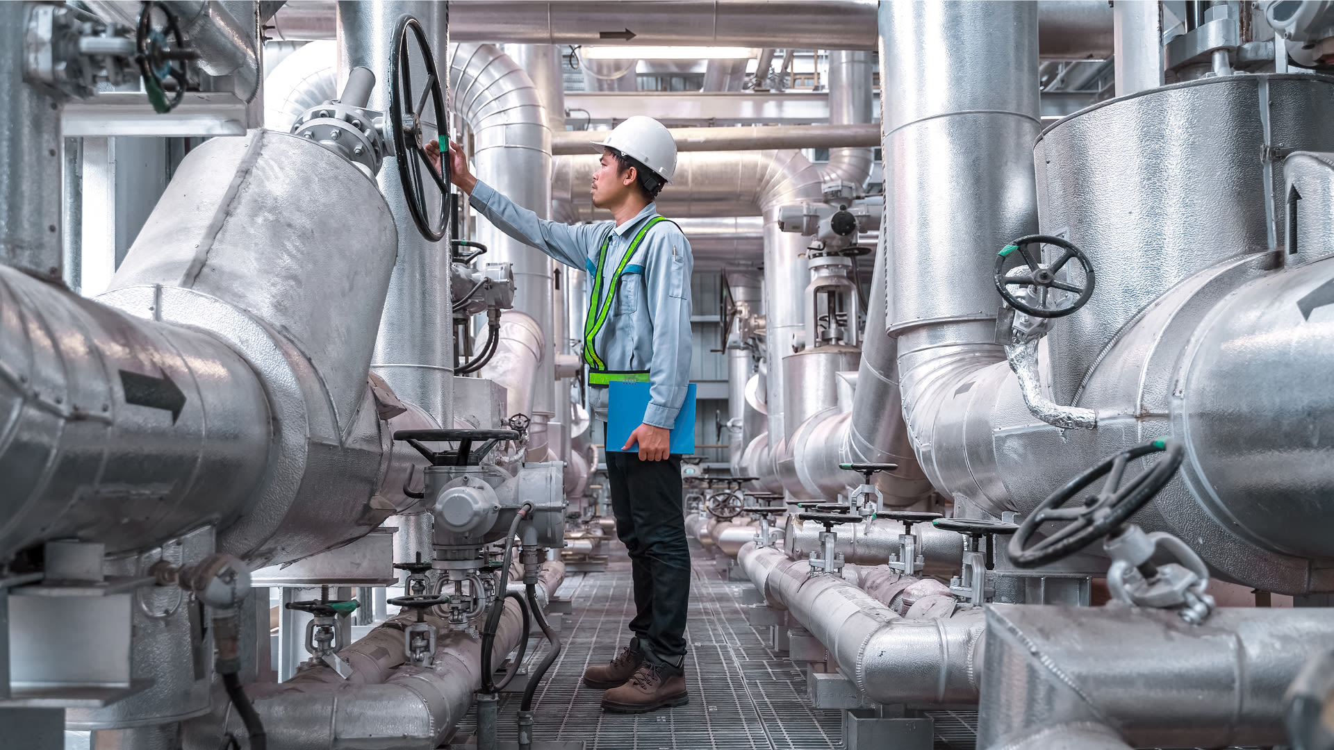 Un collaborateur inspecte les conduites et les vannes d’une installation industrielle de chaleur et d’énergie.