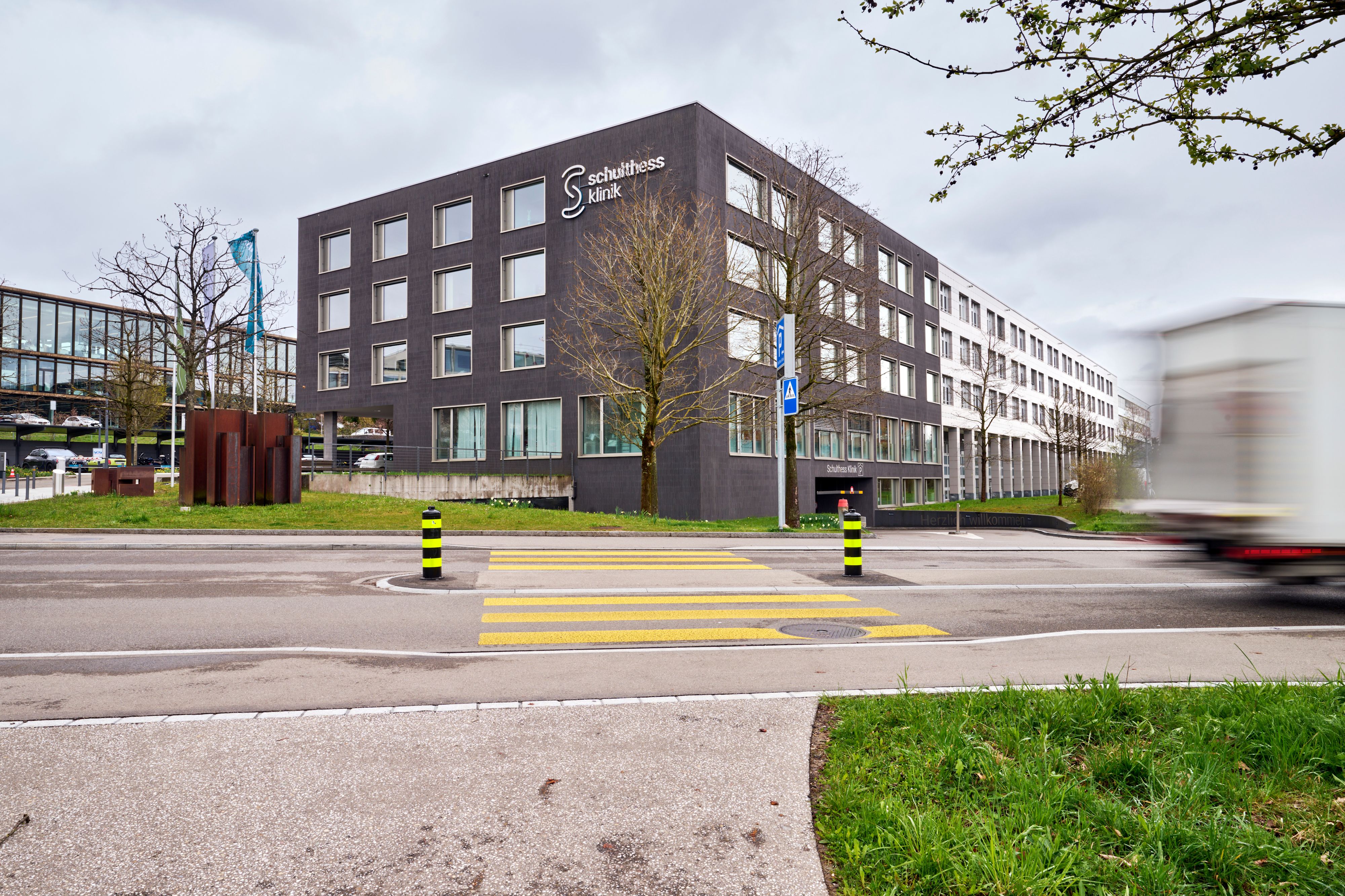 Vue extérieure de la clinique Schulthess moderne au bord d’une rue avec passage piéton.
