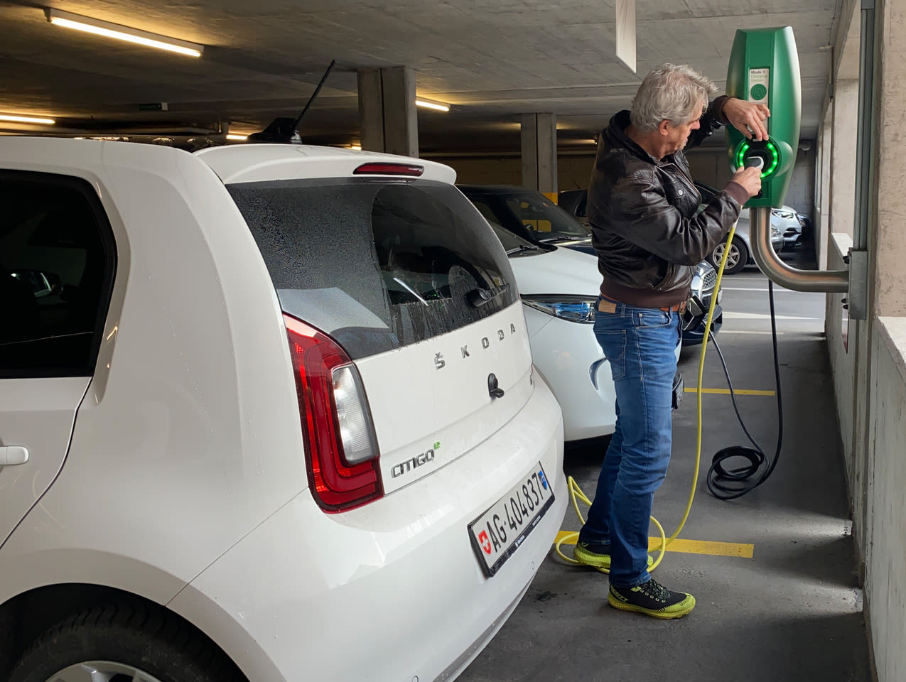 Mann schliesst Elektroauto an Ladestation an.