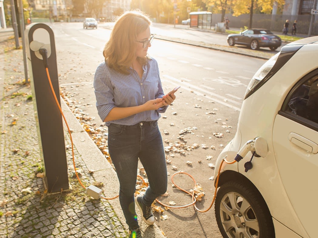 Frau schaut auf Mobiltelefon und läuft zum ladende Auto.