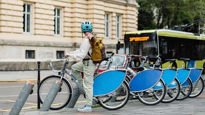 Una donna su una bici in bike sharing aspetta che passi l'autobus.