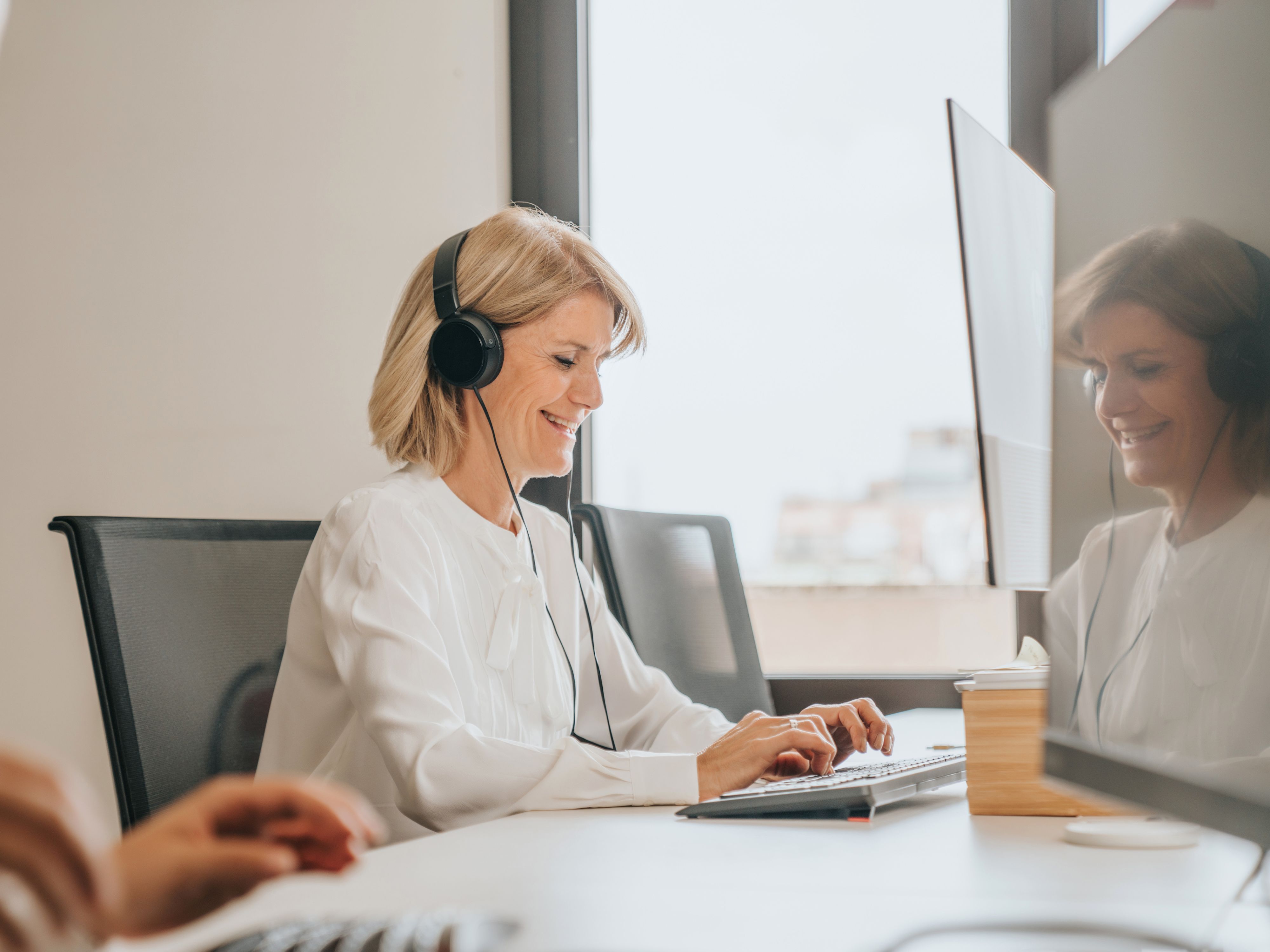 Une femme est assise devant son ordi avec des écouteurs et tape sur le clavier.