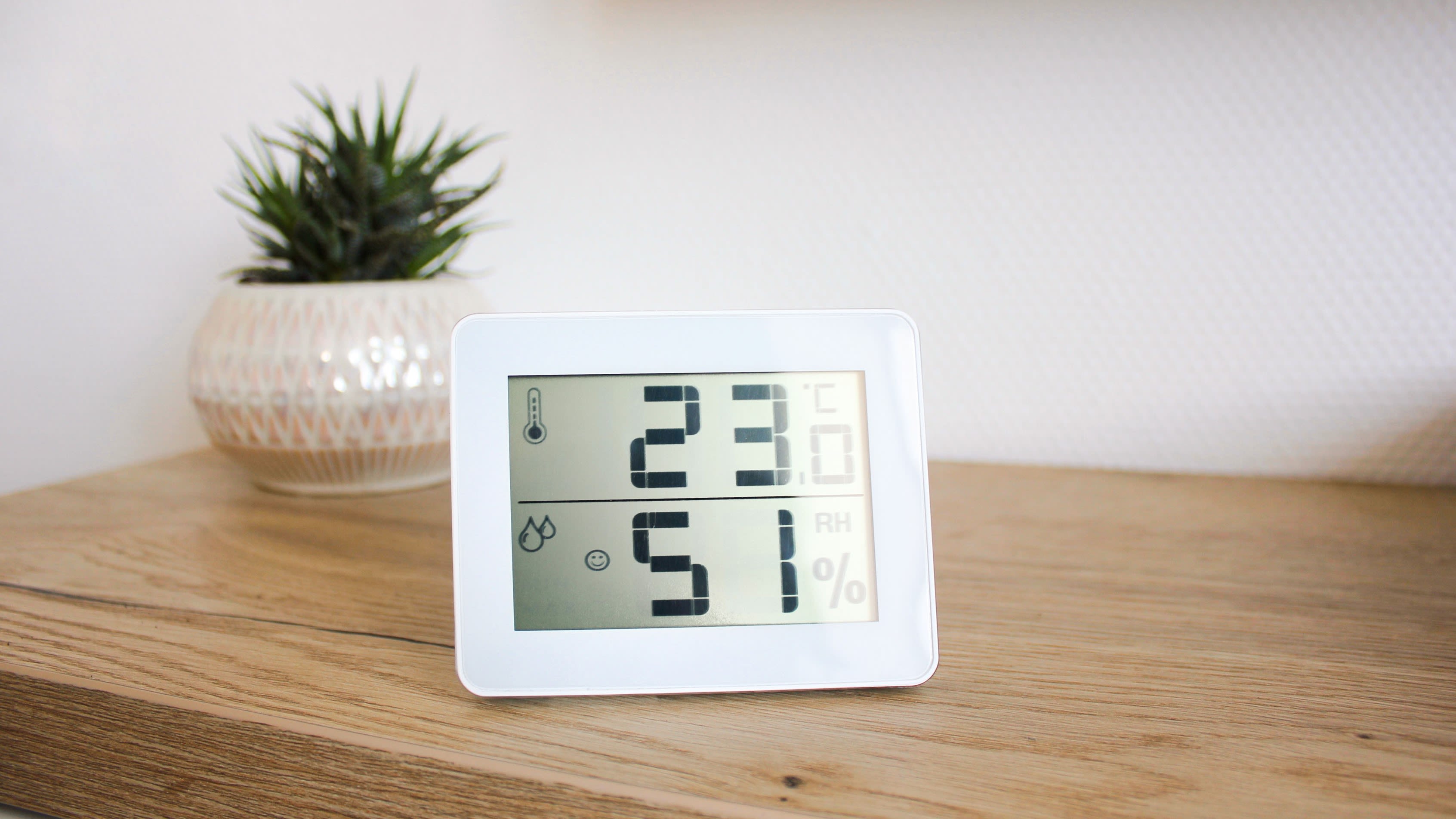 Un thermo-hygromètre numérique est posé sur une commode en bois.