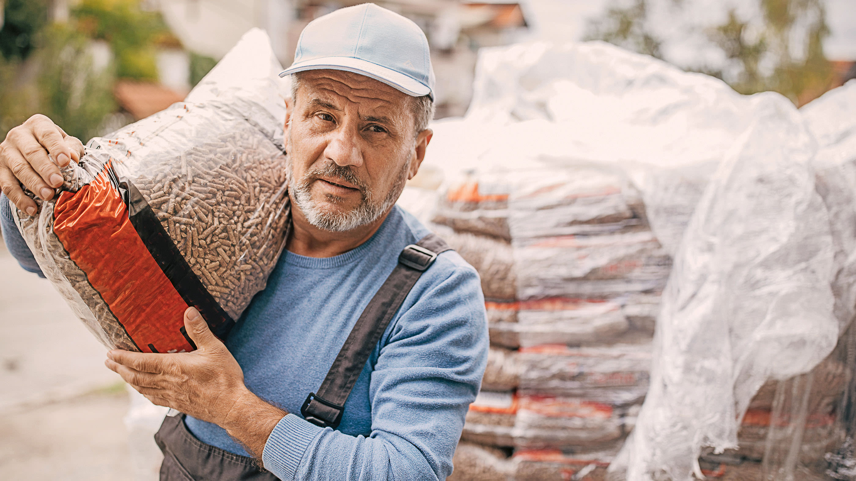 Un homme âgé porte un sac de pellets de bois sur les épaules.