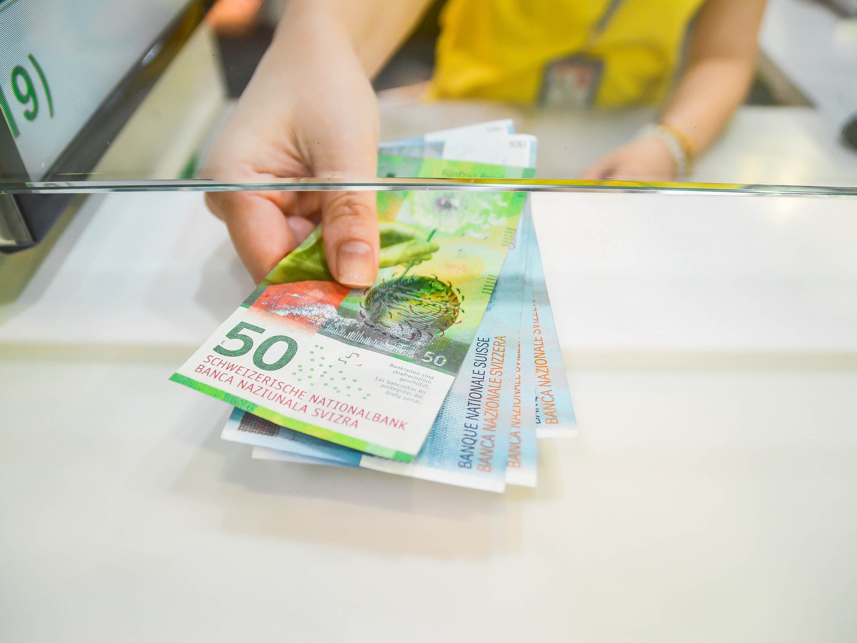 Person streckt Schweizer Banknoten ins Bild.
