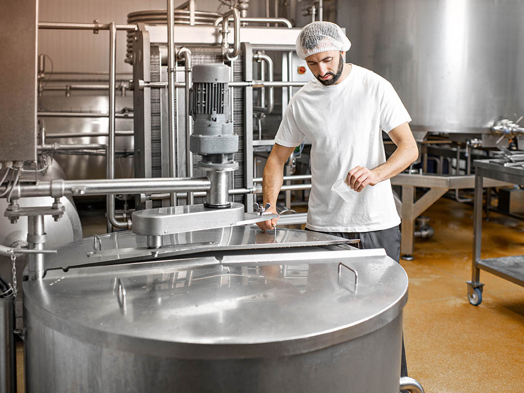 Ouvrier en uniforme près d'une cuve en acier inoxydable dans une entreprise de l'industrie alimentaire