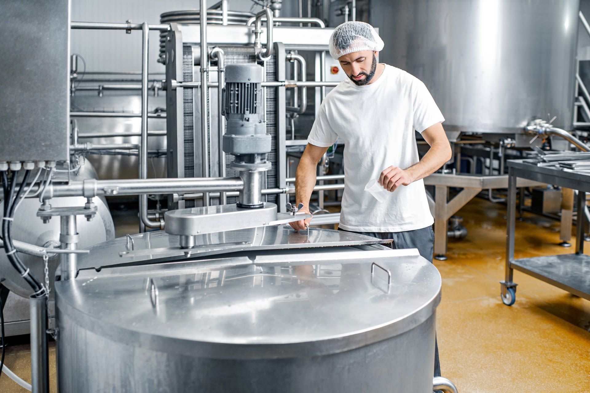 Ouvrier en uniforme près d'une cuve en acier inoxydable dans une entreprise de l'industrie alimentaire