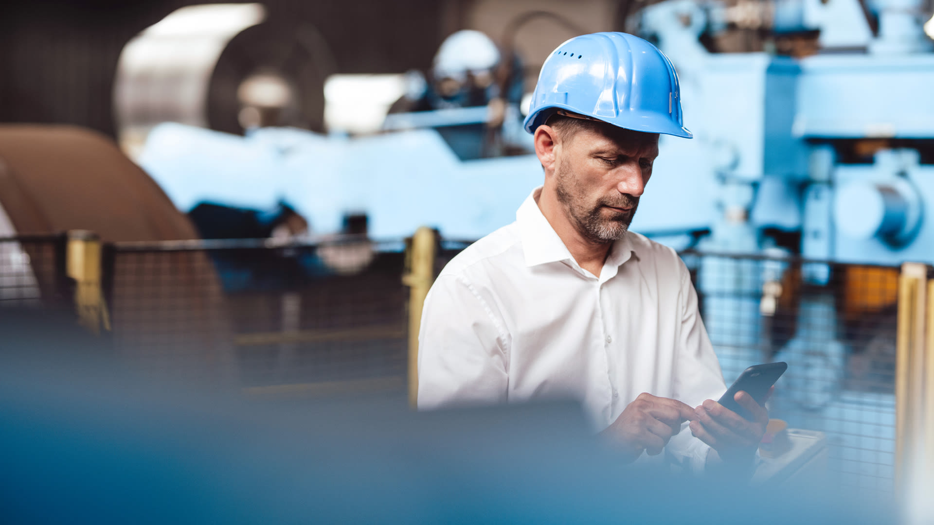 Collaboratore con casco di sicurezza utilizza uno smartphone per monitorare gli impianti di produzione.