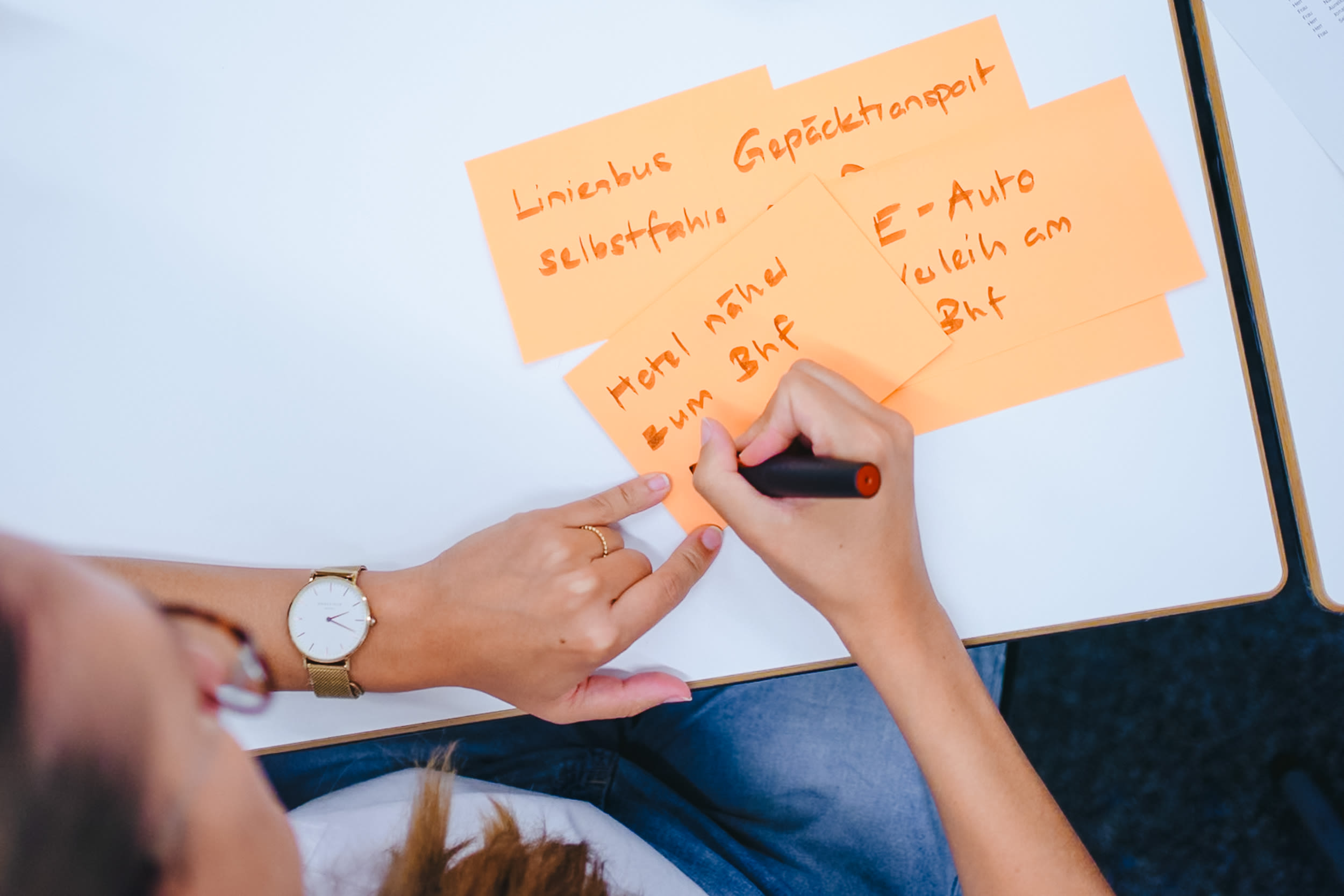 Personne écrivant des idées sur des notes adhésives orange lors d'un atelier de Design Thinking