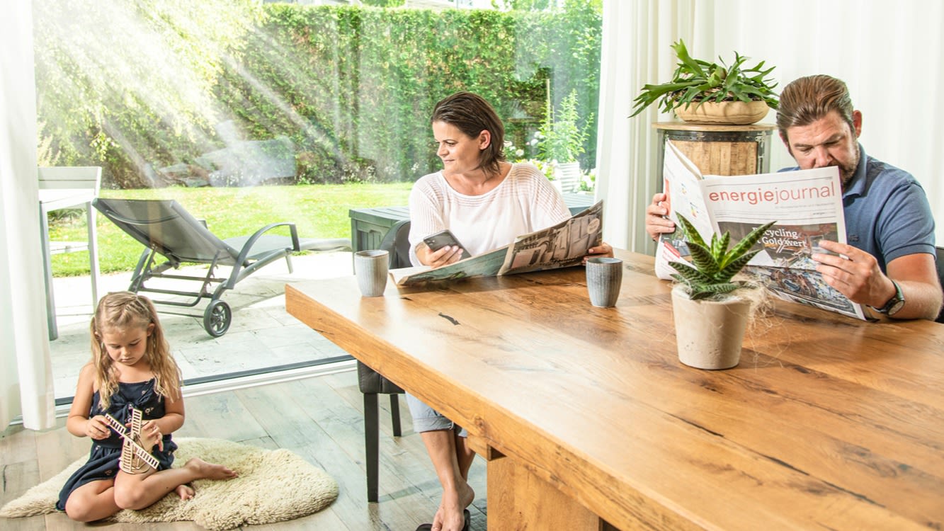 Un homme est assis à la table et lit le journal de l'énergie. Une femme et une fille sont assises à côté de lui.
