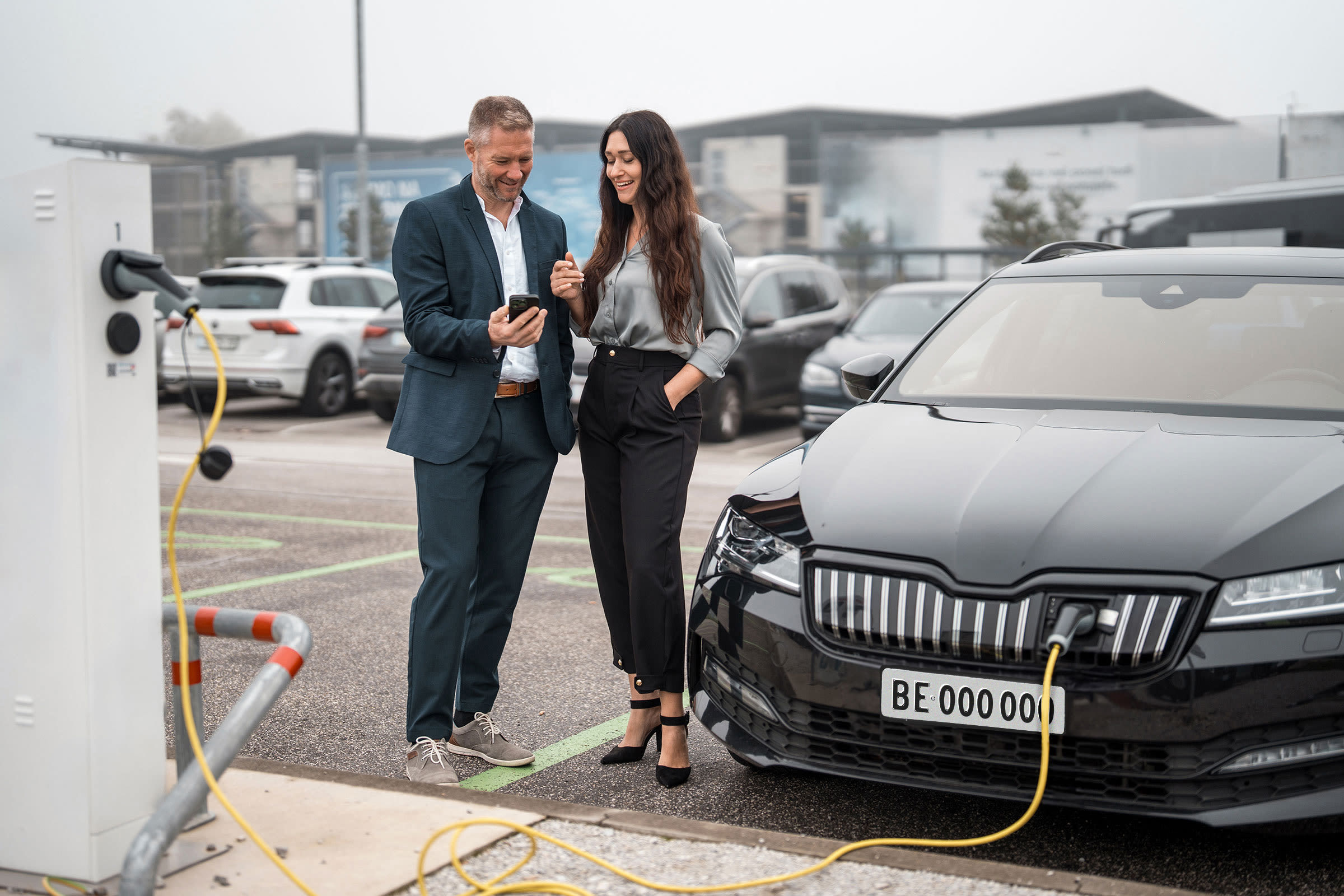 Zwei Personen im Business-Look laden ein E-Auto.