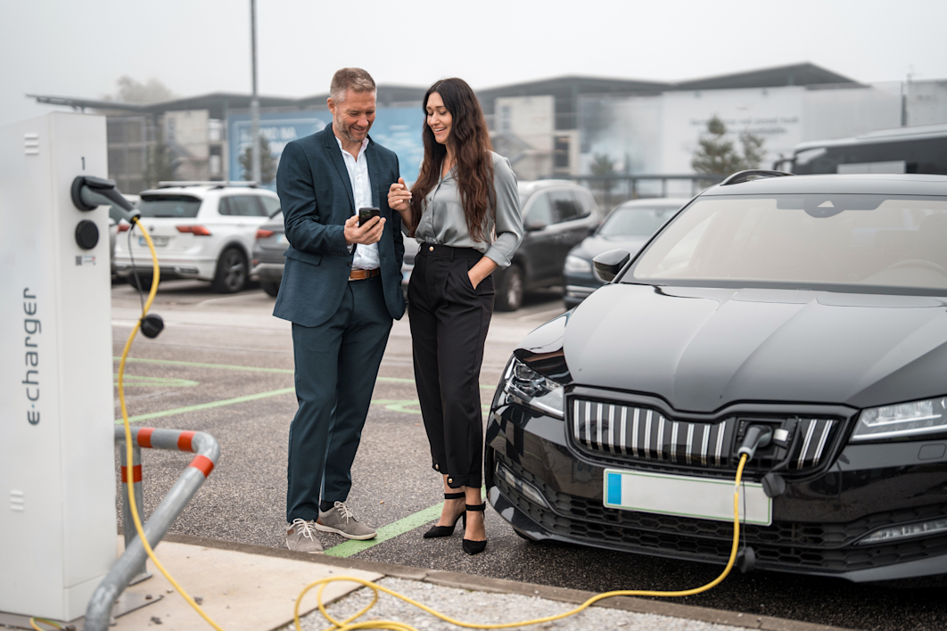 Zwei Personen im Business-Look laden ein E-Auto.