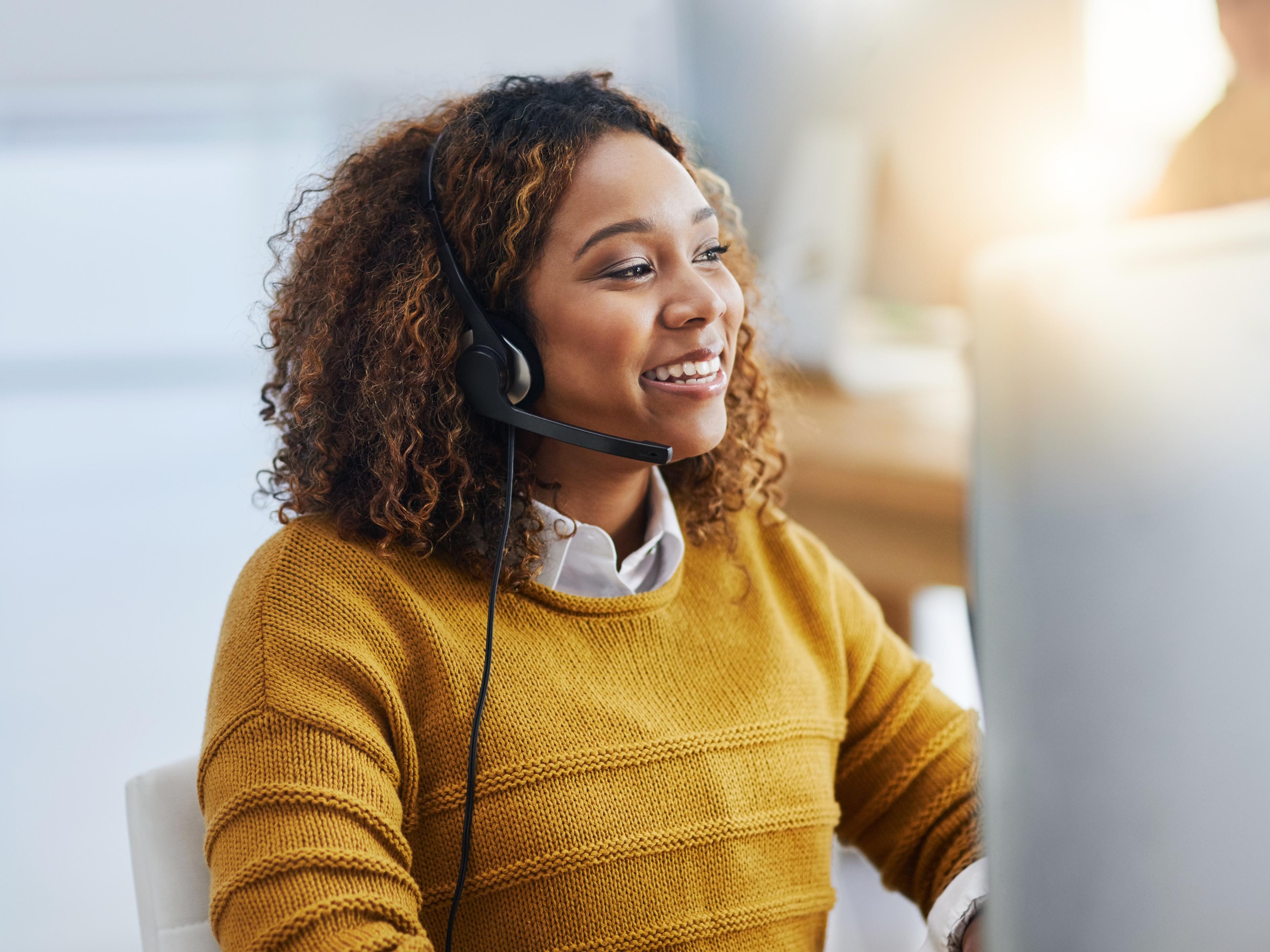Une femme devant son ordinateur parle à ses clients avec un casque.