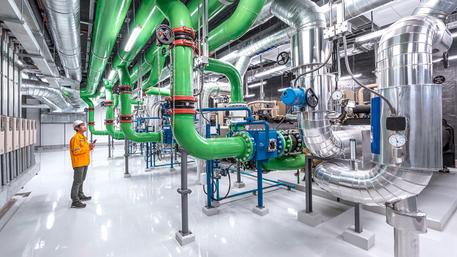 Mitarbeitender überwacht technische Anlage mit Rohrleitungen und Maschinen zur industriellen Wärme- und Energieversorgung.