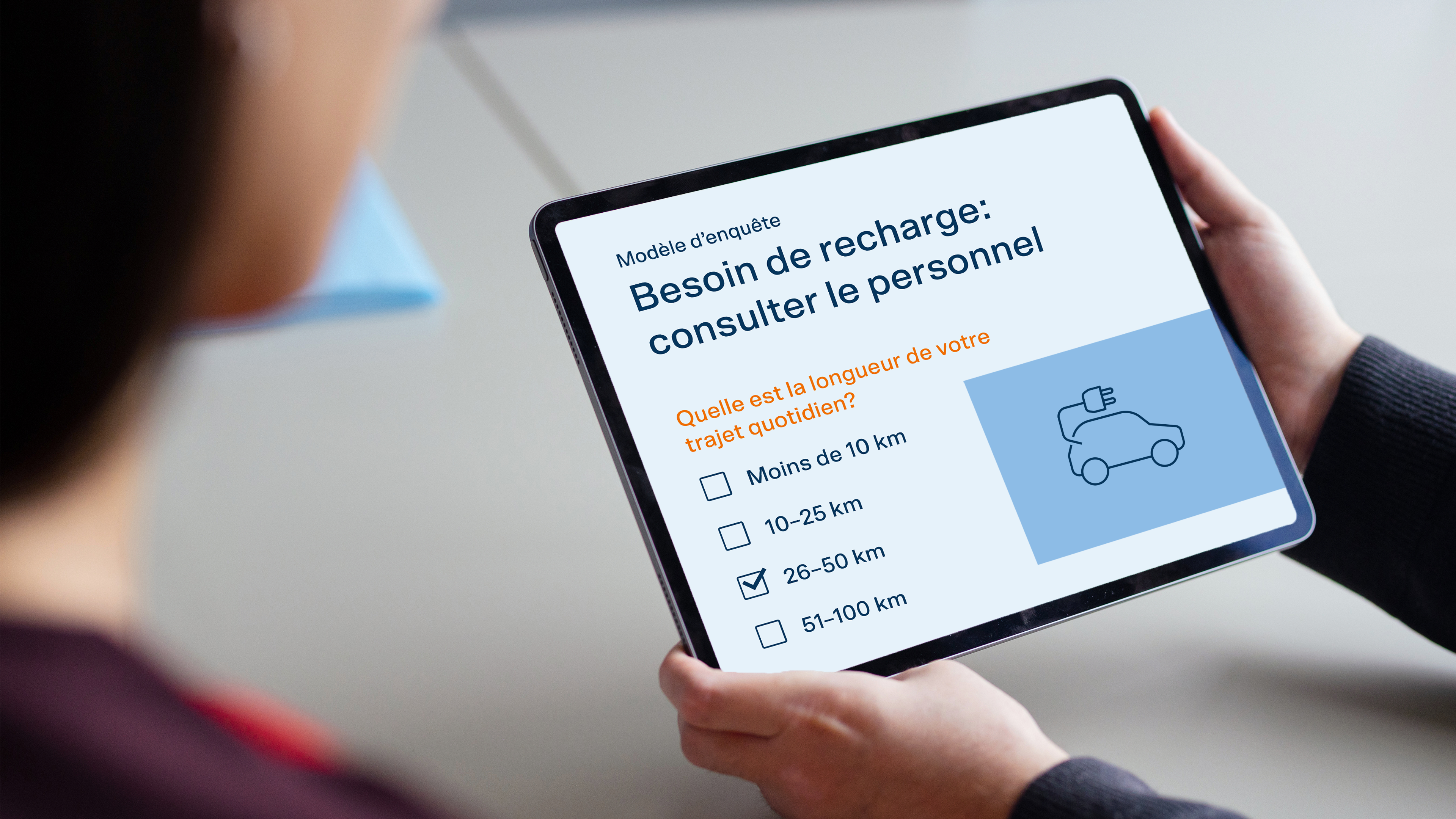 Une personne tient dans sa main une tablette sur laquelle s'affiche l'enquête.