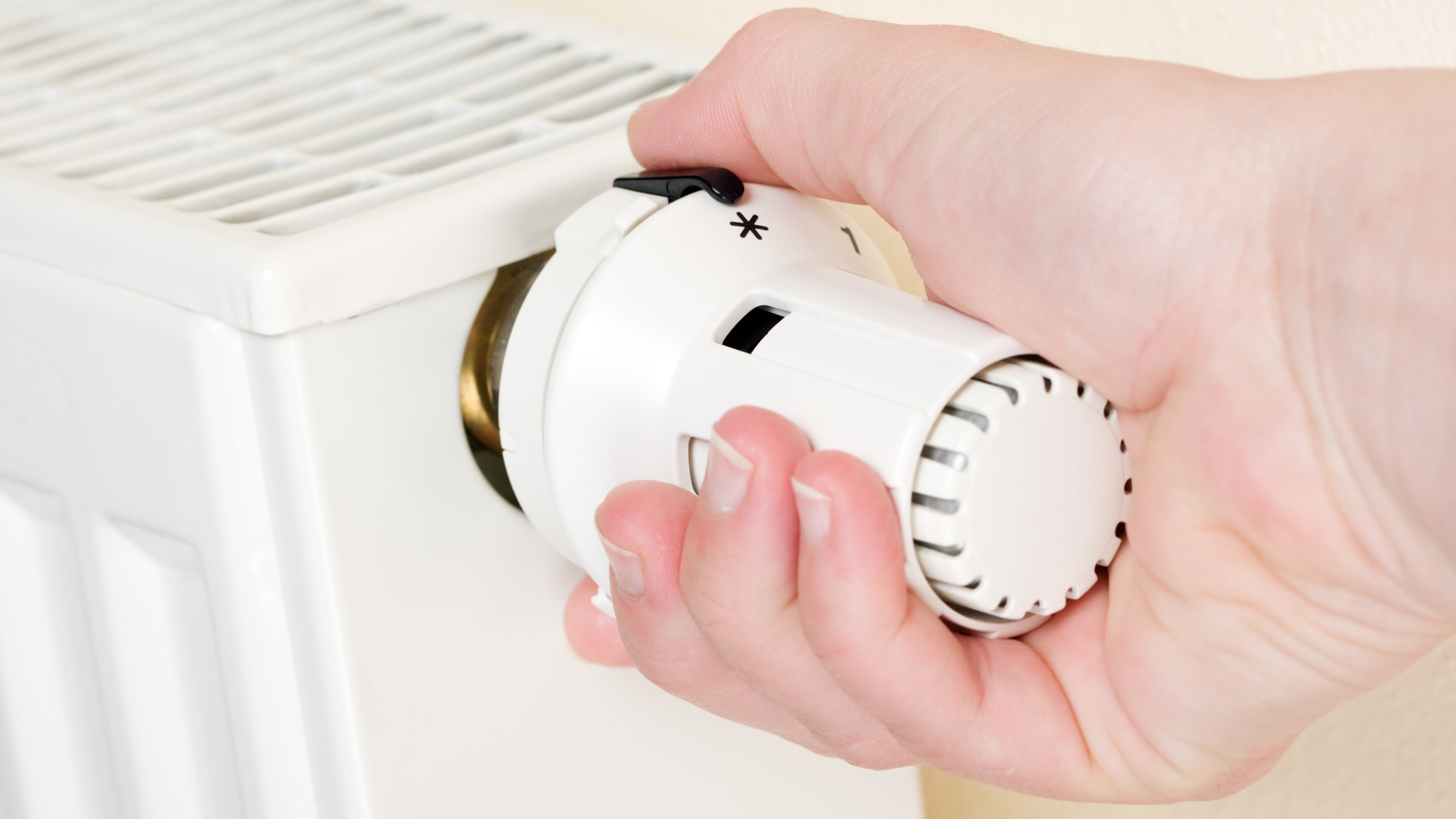 Une personne règle la température ambiante sur la vanne thermostatique d'un radiateur