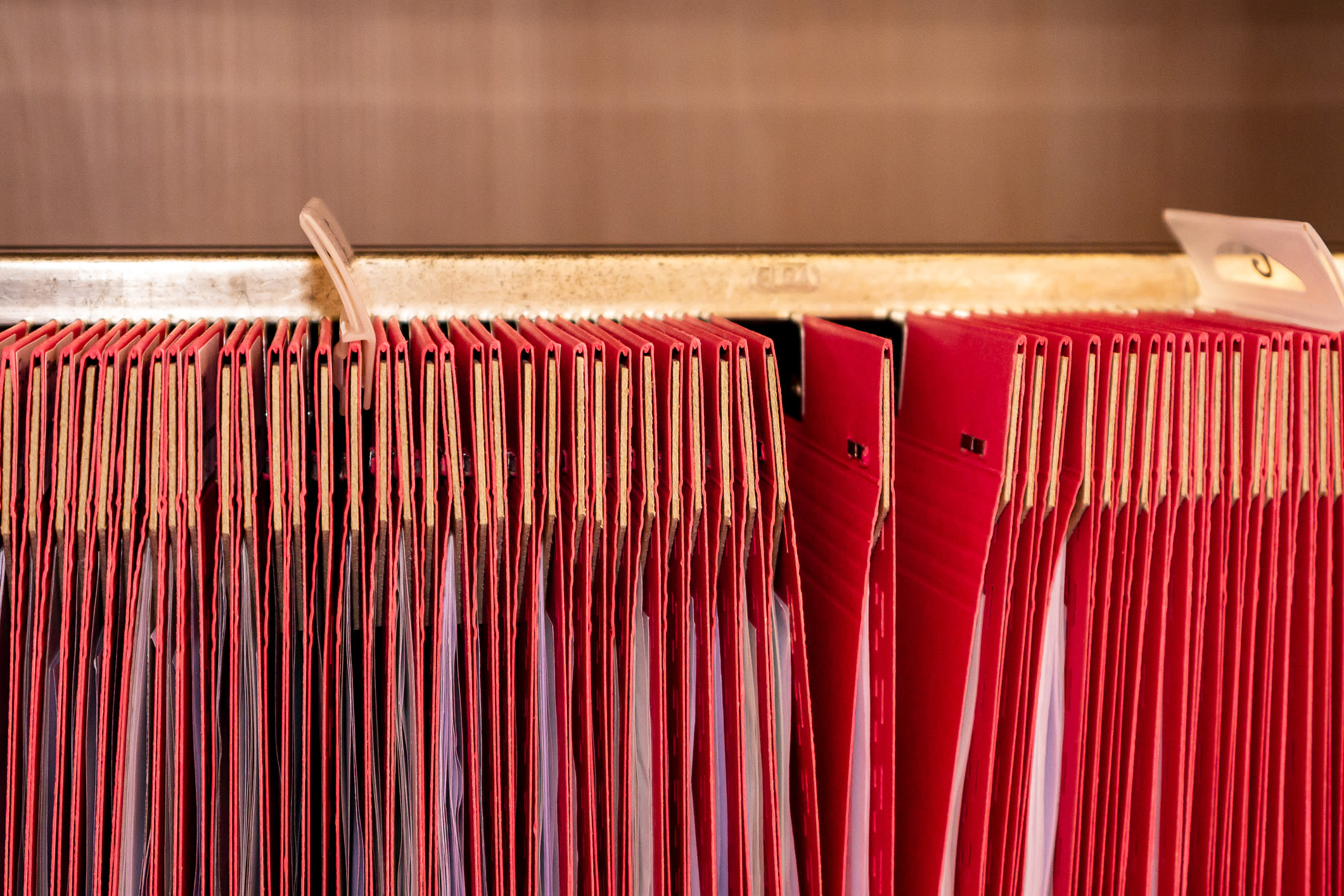 Cartelle sospese rosse con documenti in un archivio.
