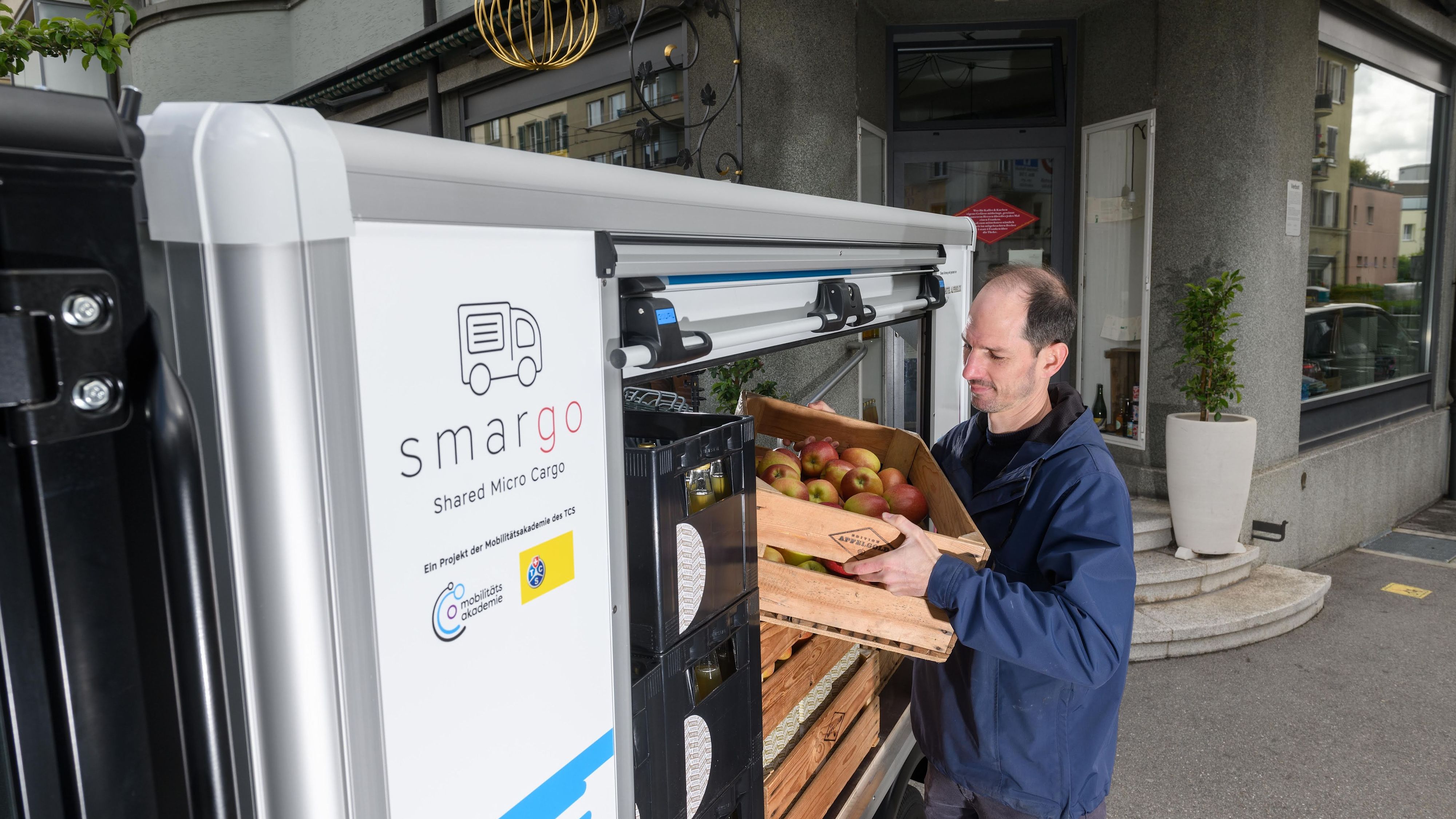 Un uomo sta caricando una cassa di mele su un furgoncino elettrico condiviso.