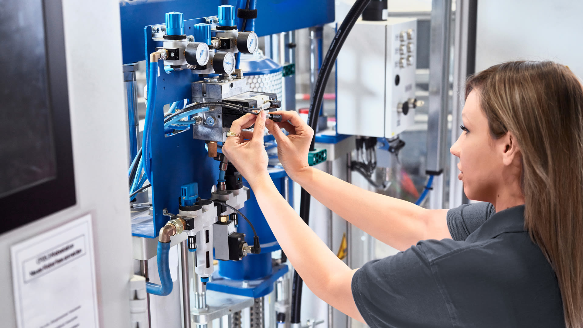 Mitarbeitende richtet eine industrielle Anlage ein und überprüft pneumatische Steuerungskomponenten.