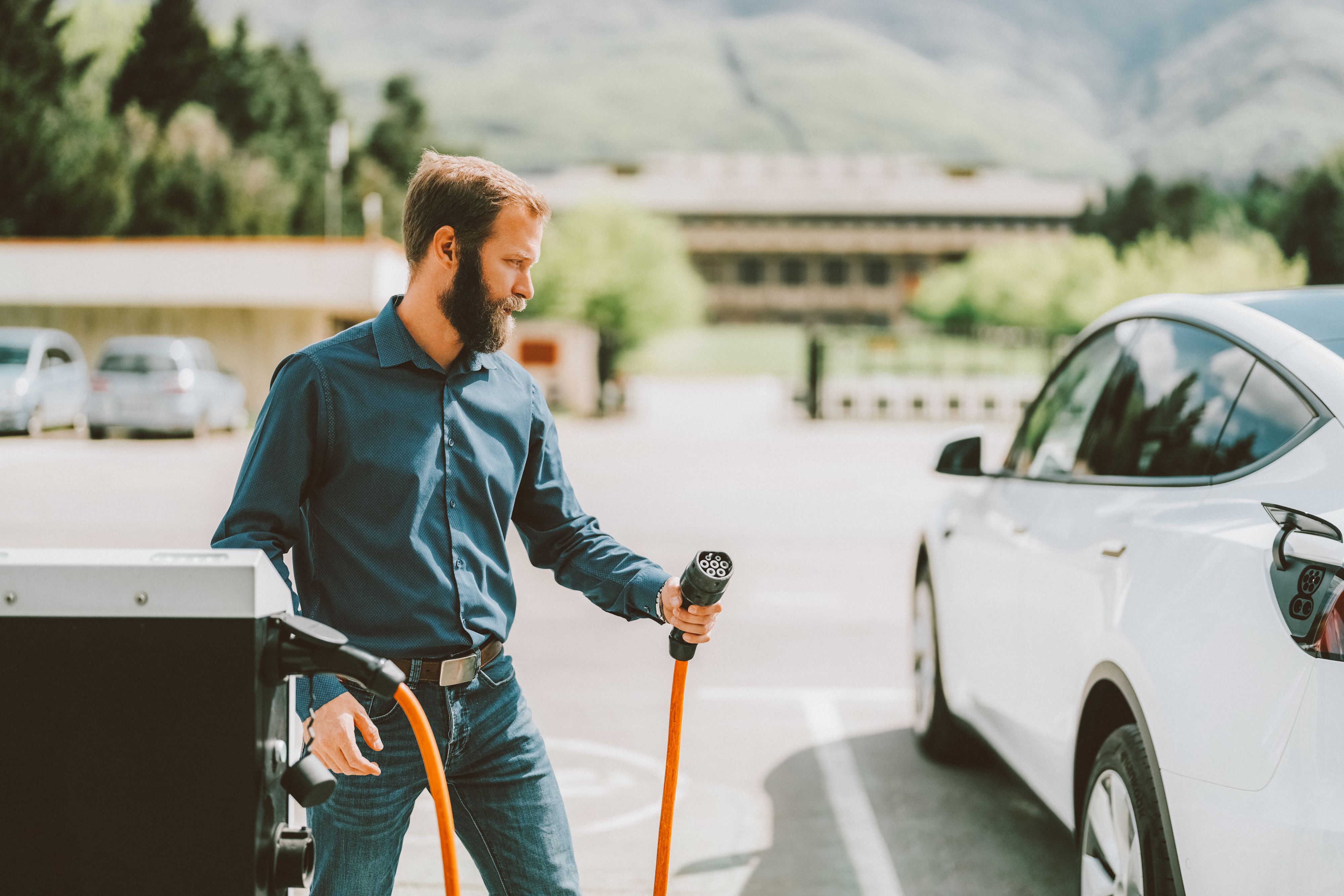 Un jeune homme en chemise recharge une voiture électrique.