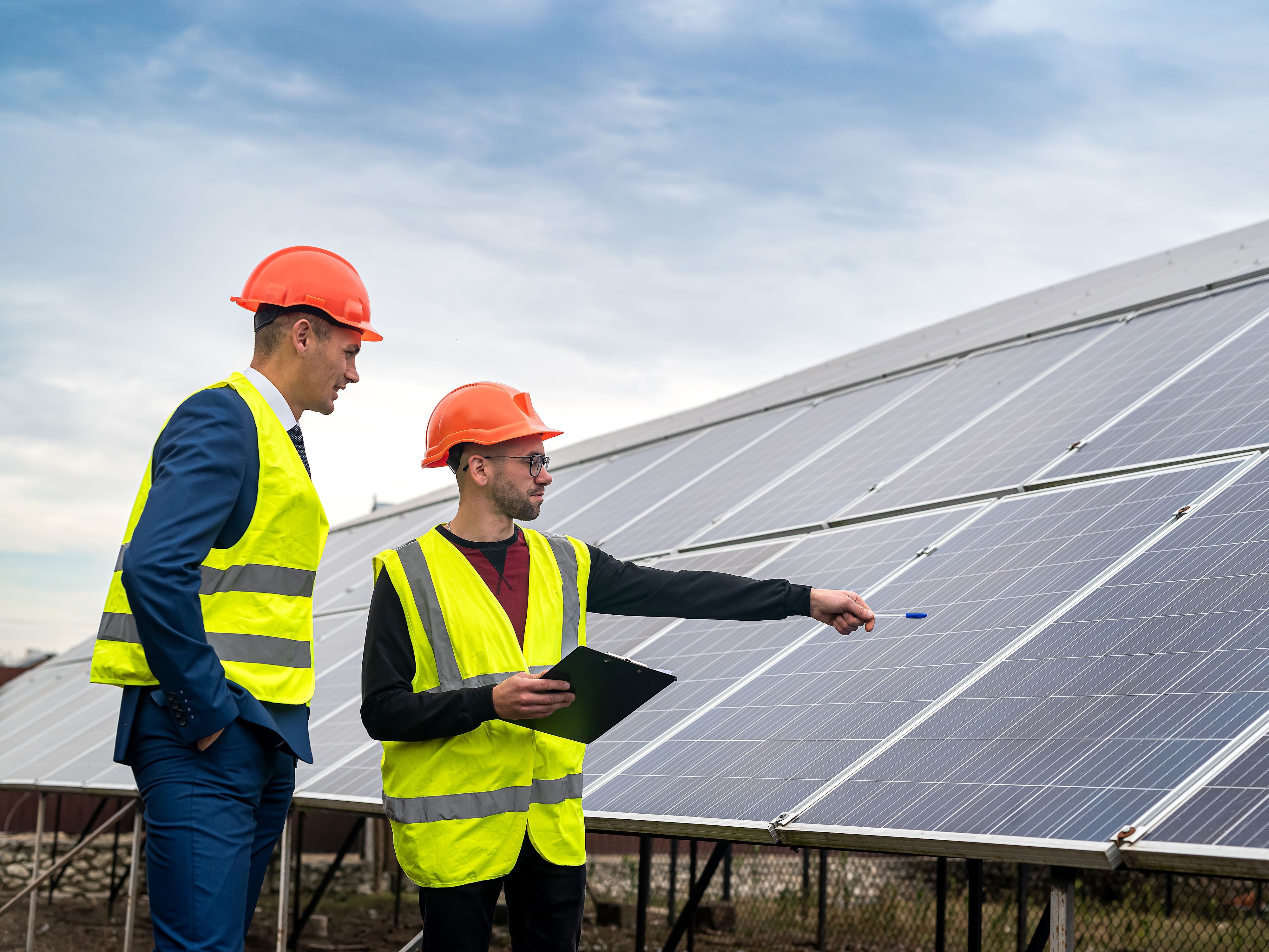 Deux hommes discutent devant une installation photovoltaïque sur un toit.