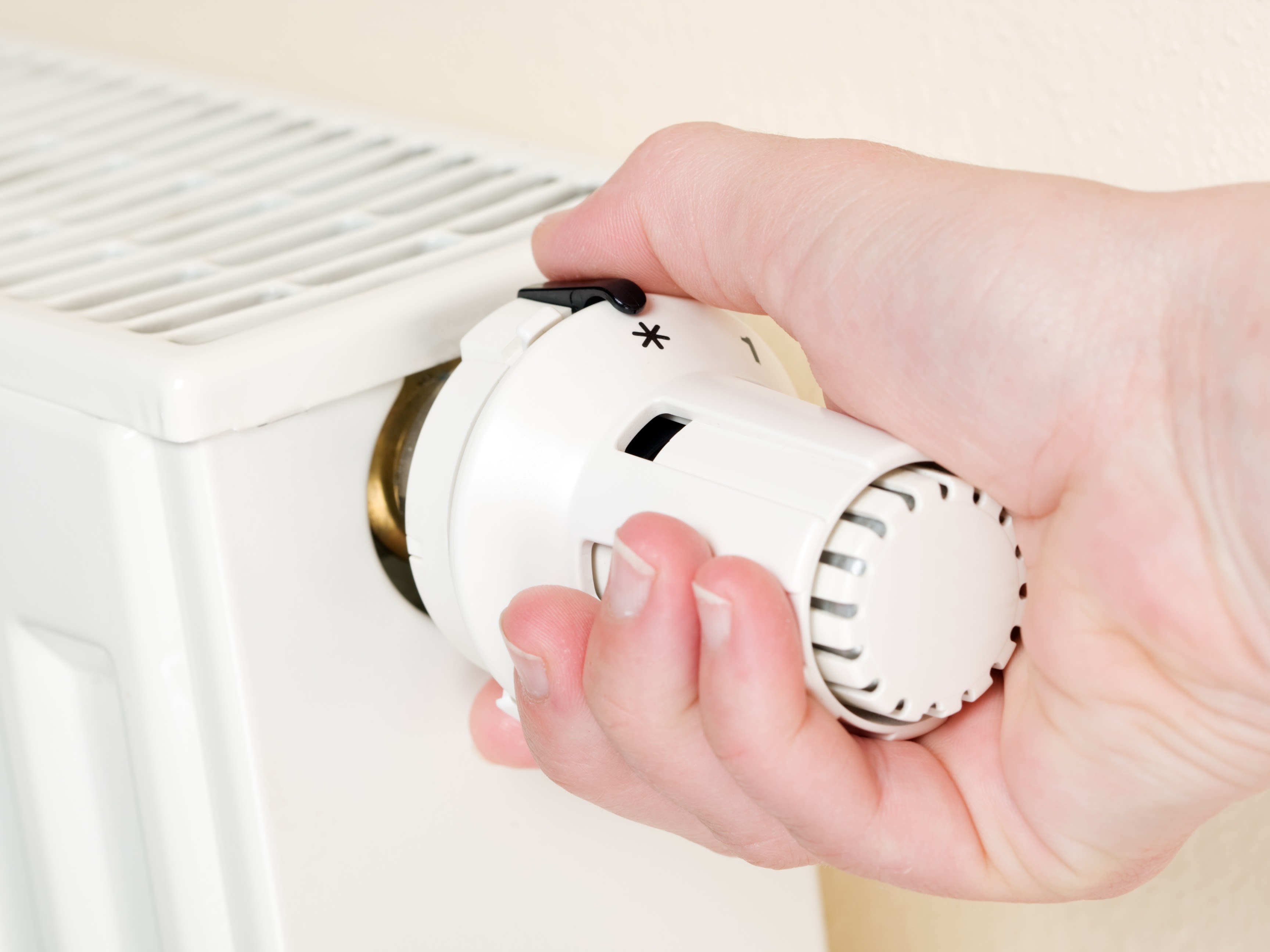 Une personne règle la température ambiante sur la vanne thermostatique d'un radiateur
