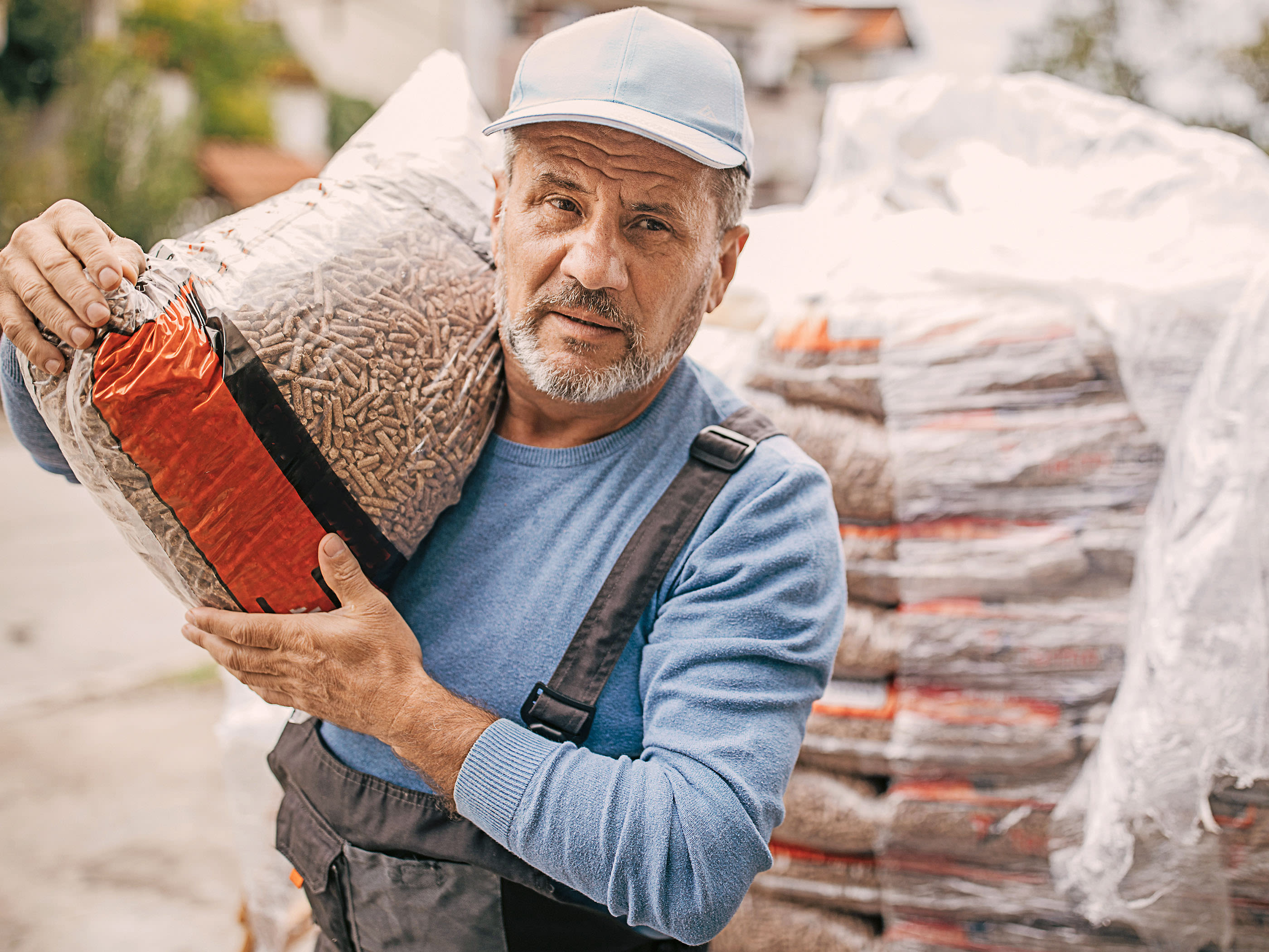 Un homme âgé porte un sac de pellets de bois sur les épaules.