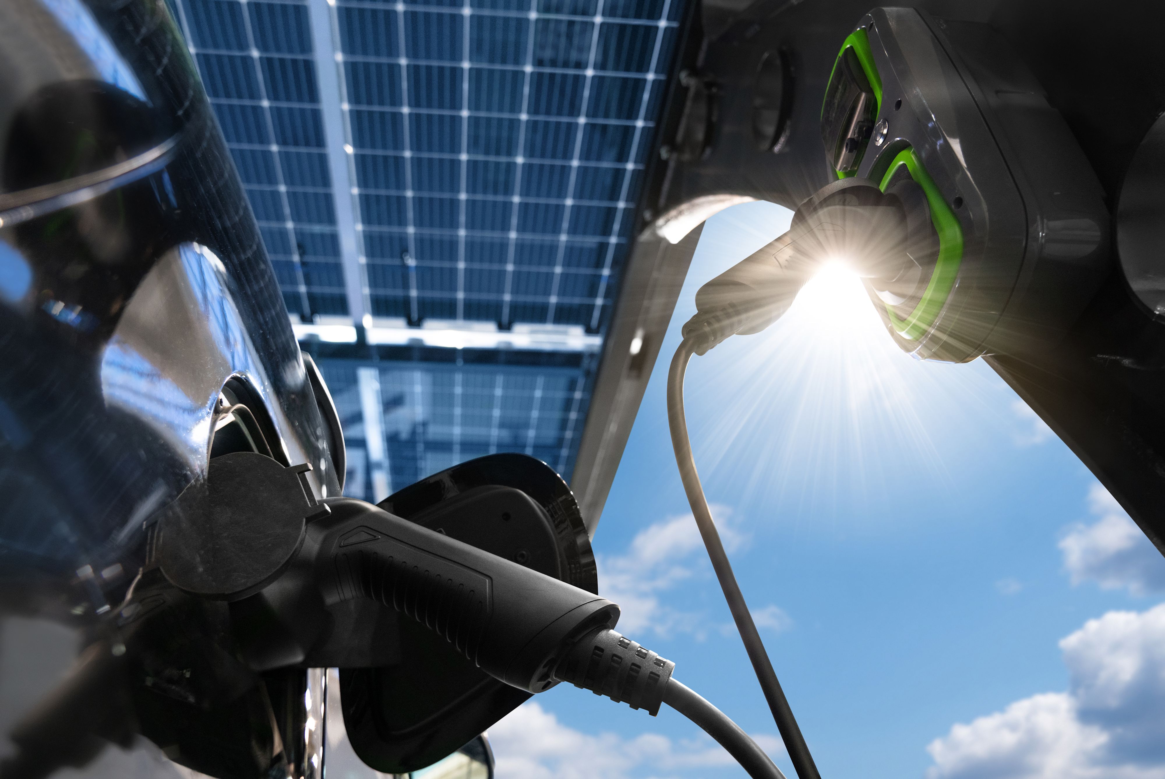 Gros plan d’une voiture électrique en charge sous des panneaux solaires par temps ensoleillé.