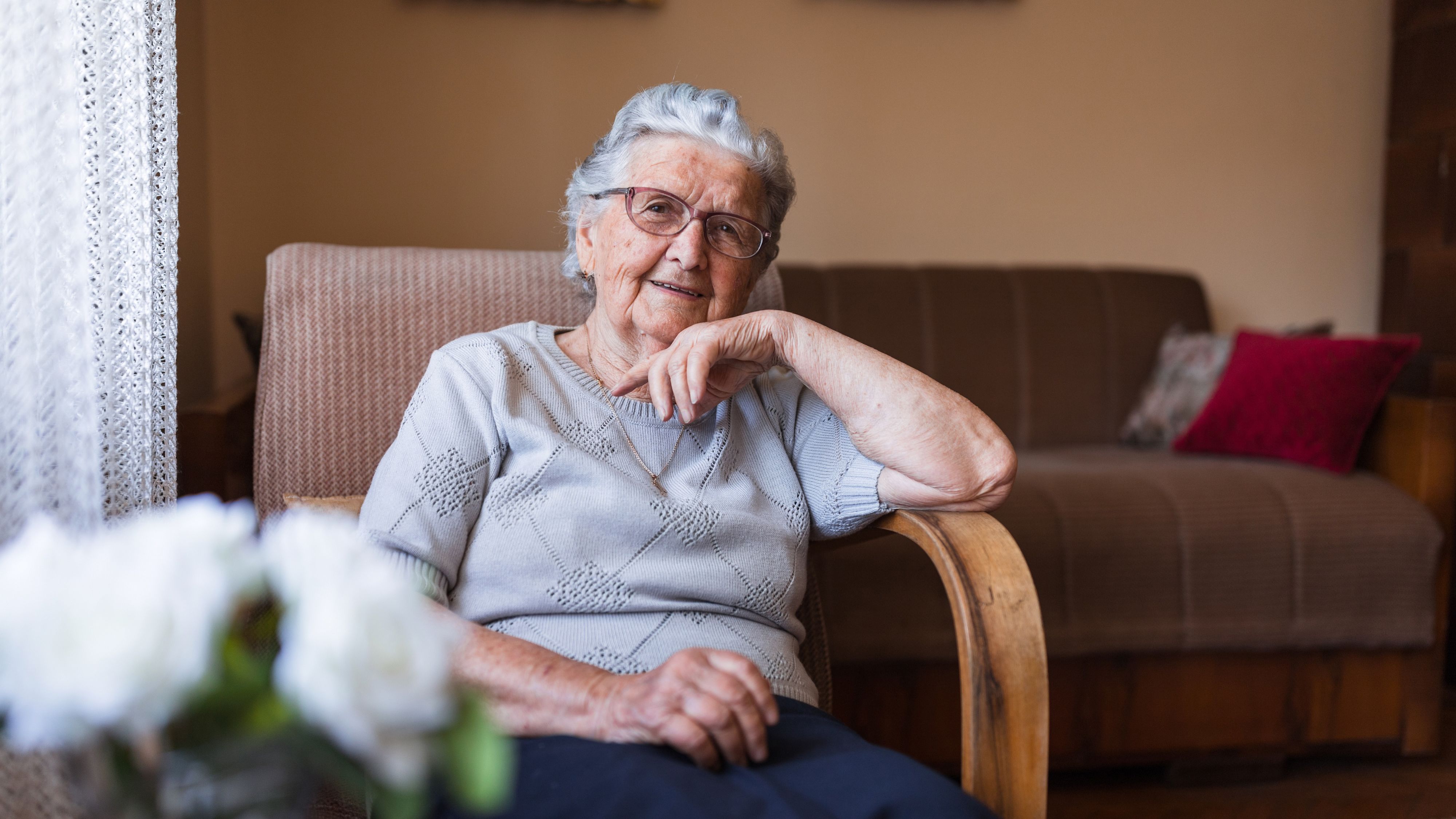 Une vieille dame est assise dans un fauteuil et sourit.