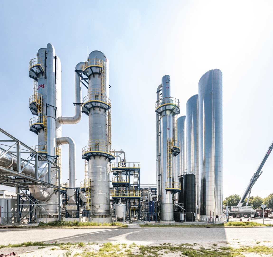 Impianto industriale delle centrali a legna di Basilea, con alte torri argentate e tubazioni sotto un cielo azzurro.