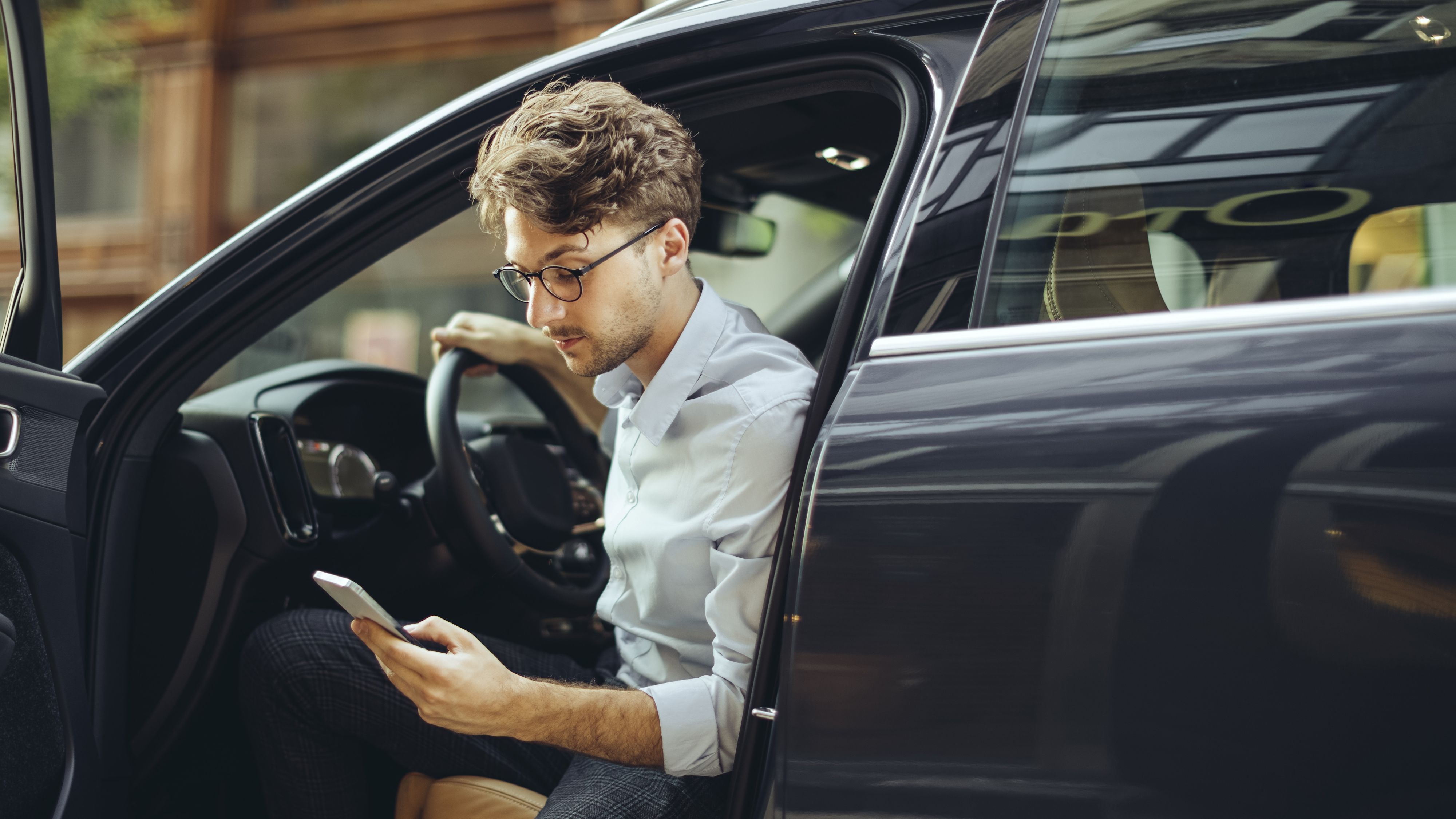 Mann mit Smartphone in de Hand steigt aus einem Elektroauto aus