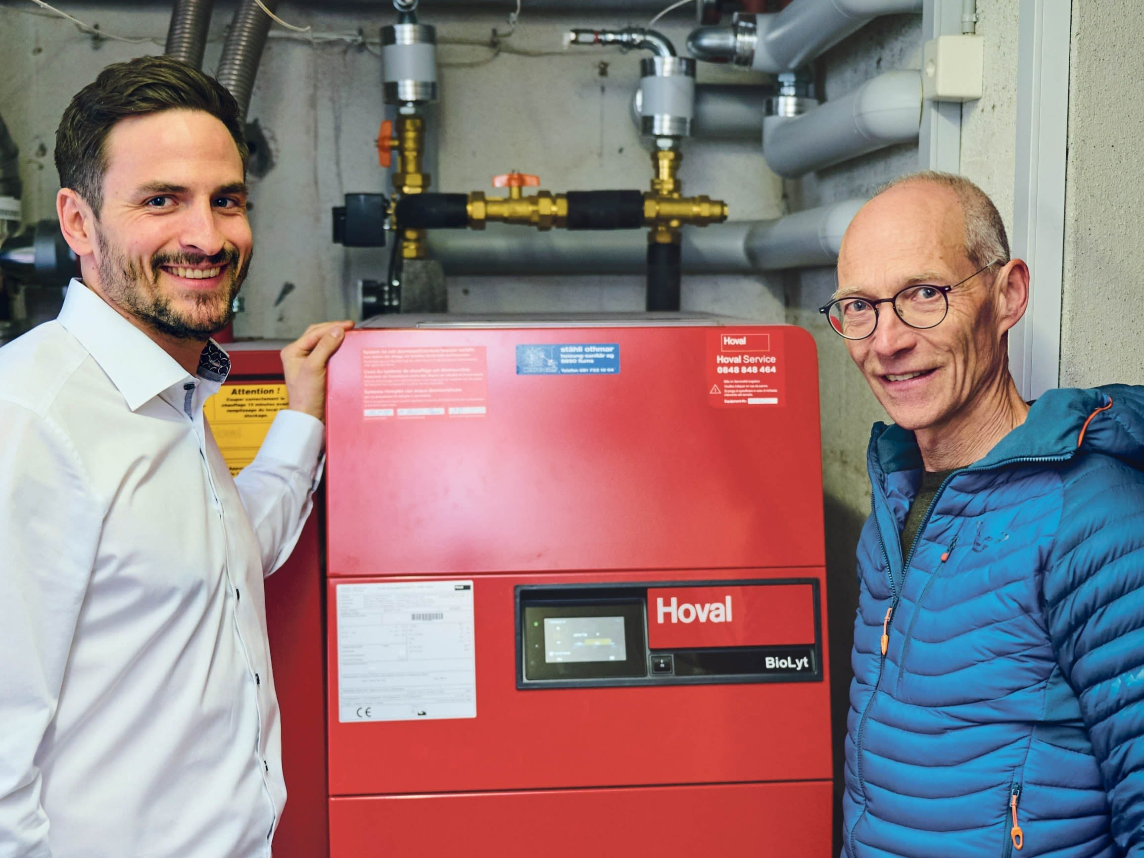 Justus Gallati et Fabian Burkhalter devant le chauffage à pellets combiné à l'énergie solaire thermique qui a remplacé le chauffage au mazout.