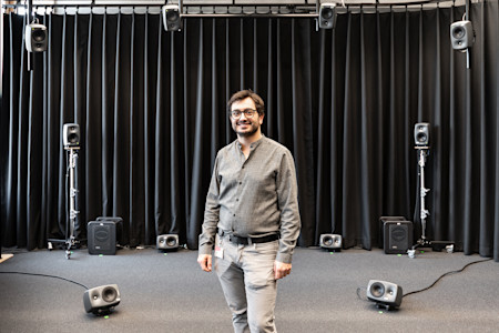 Sascha Etezazi, KIO’s Artistic Research Associate in Composition & Sound Design, stands in front of the Genelec immersive system.