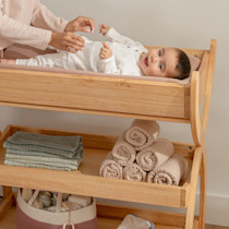 Baby lying on changing table with caregiver arranging clothing