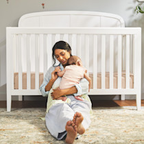 Person sitting on floor with baby in crib, white crib in background