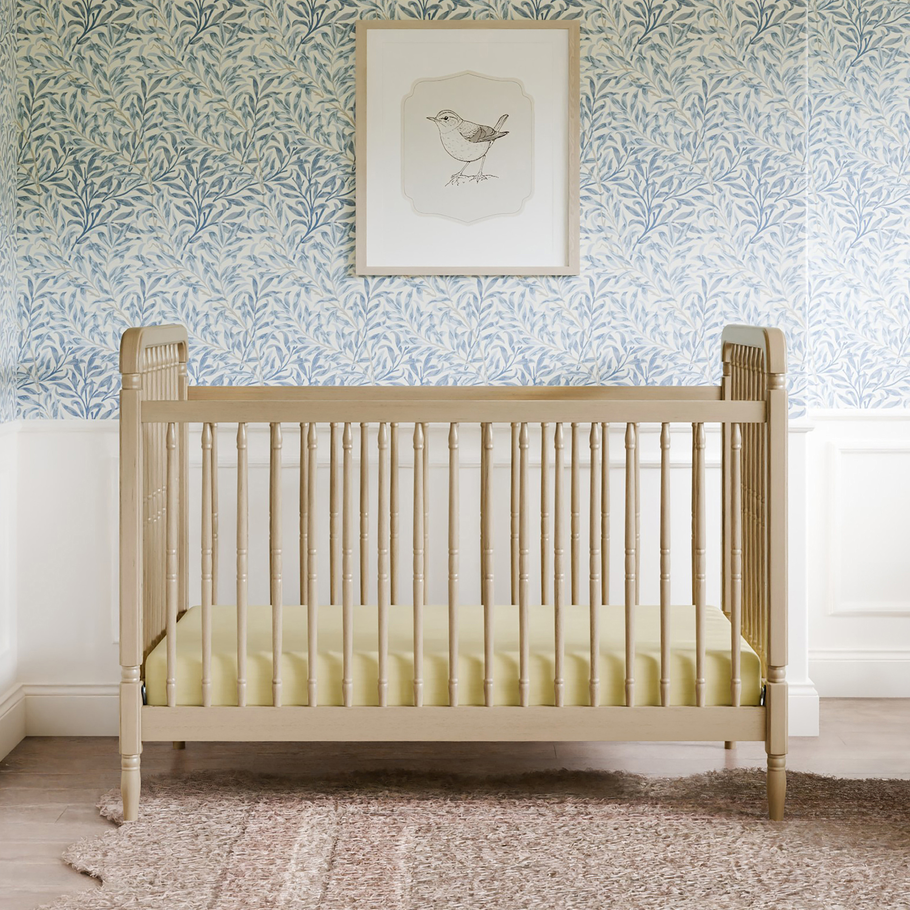 Wooden spindle crib with yellow bedding in a nursery.