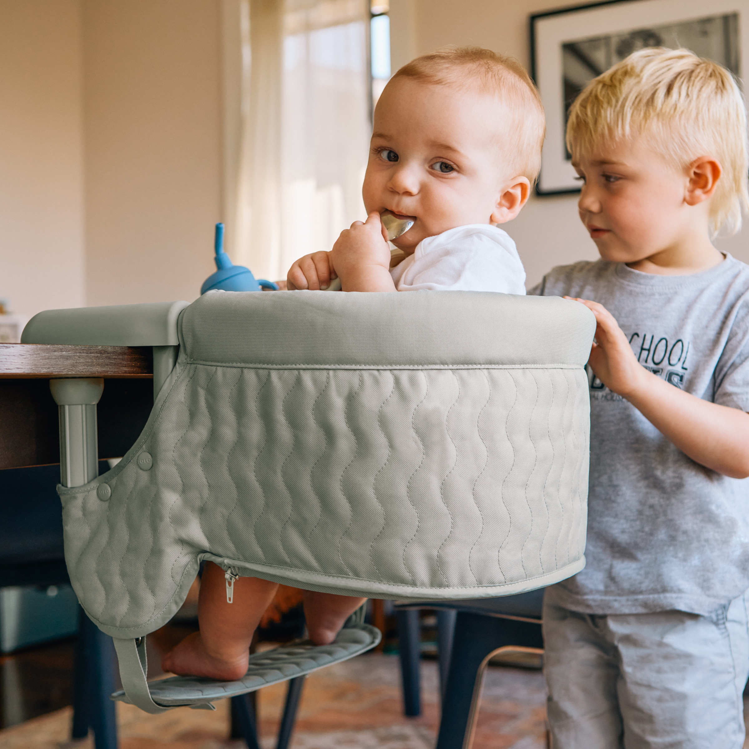 Baby eating in a quilted grey high chair with family members.