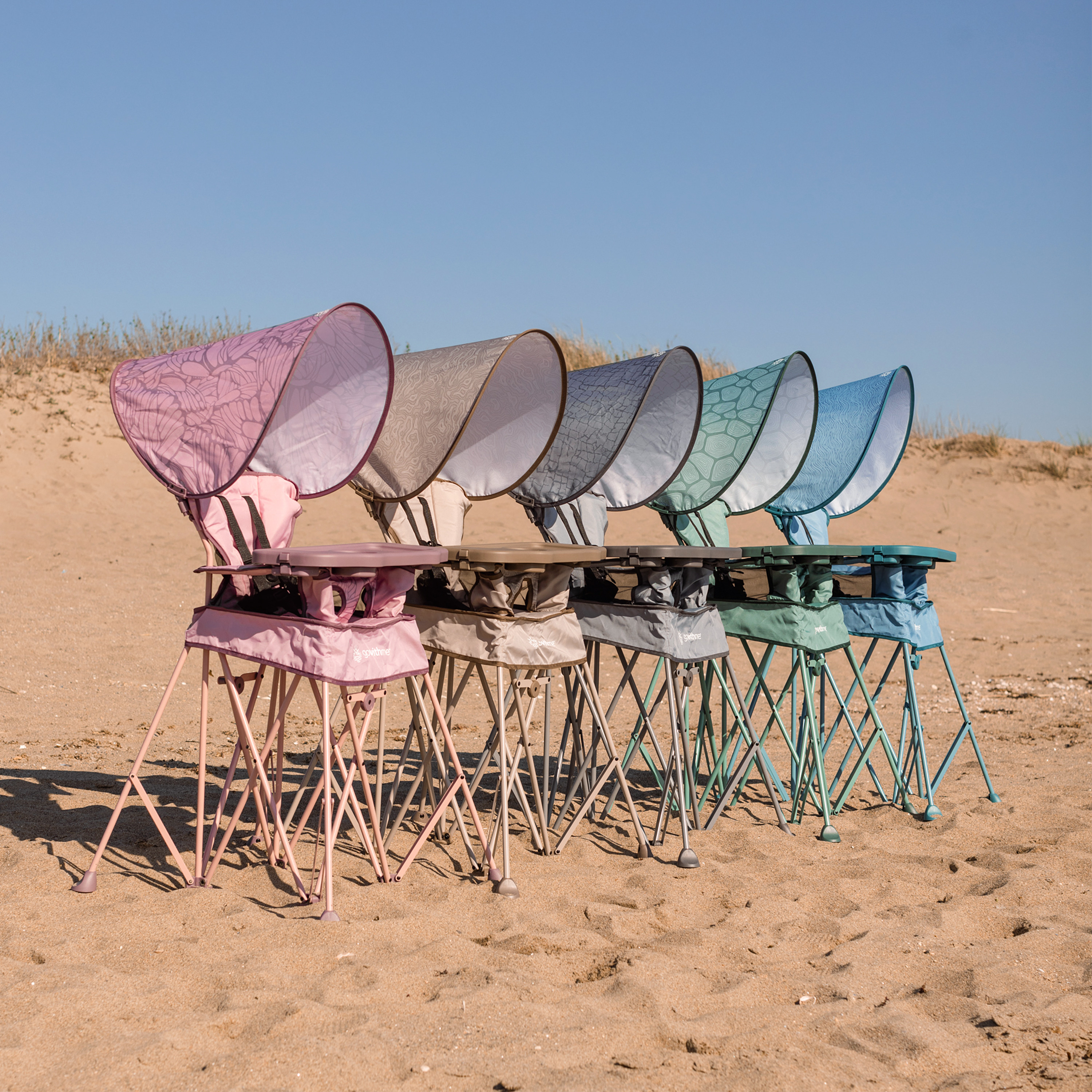 Group of portable high chairs in pink, grey, and teal colors set up.