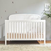 White crib in a nursery setting with headboard and rails