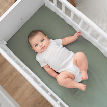 Baby lying in white wooden bassinet with green fitted sheet