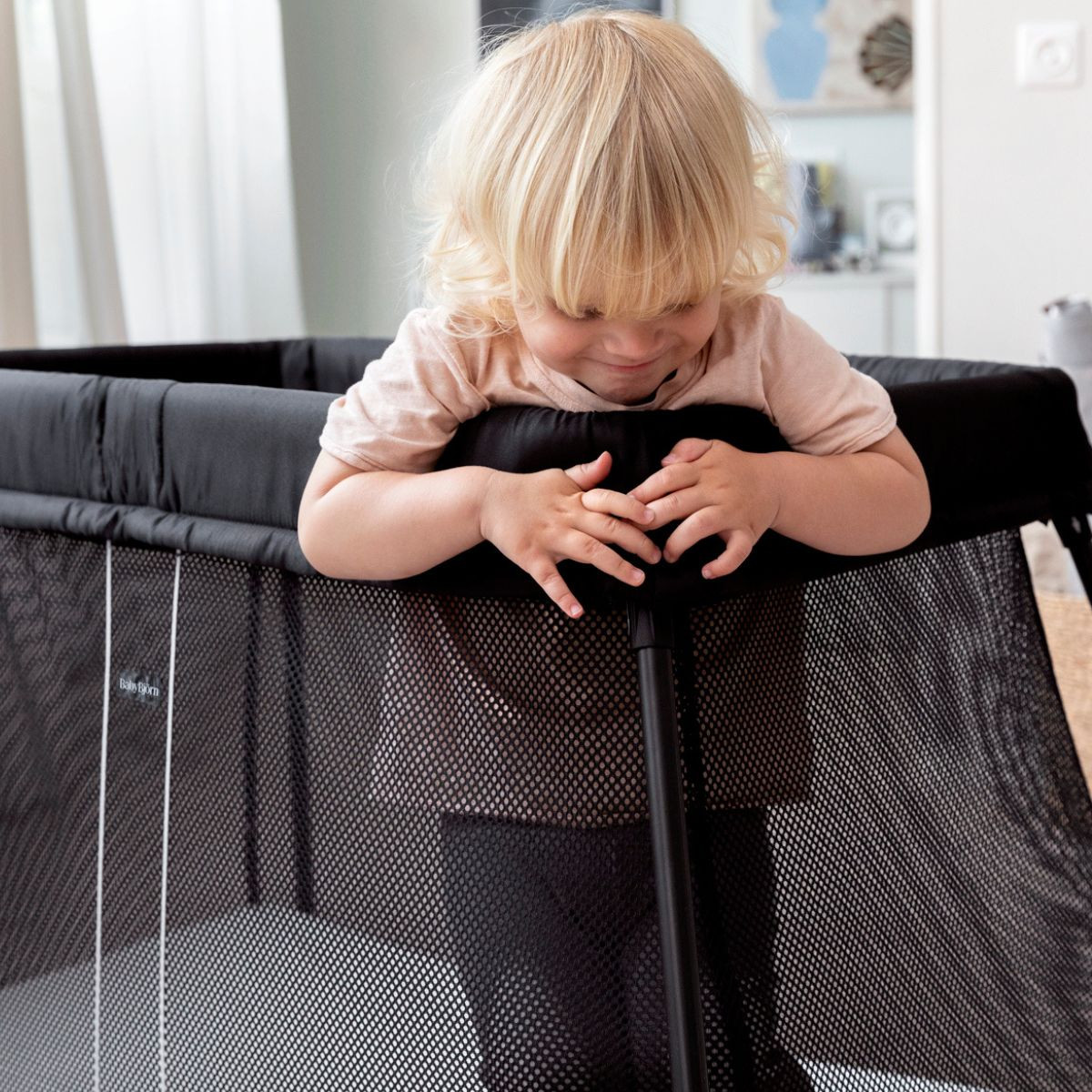 A young child touching the fabric cover of the travel crib.
