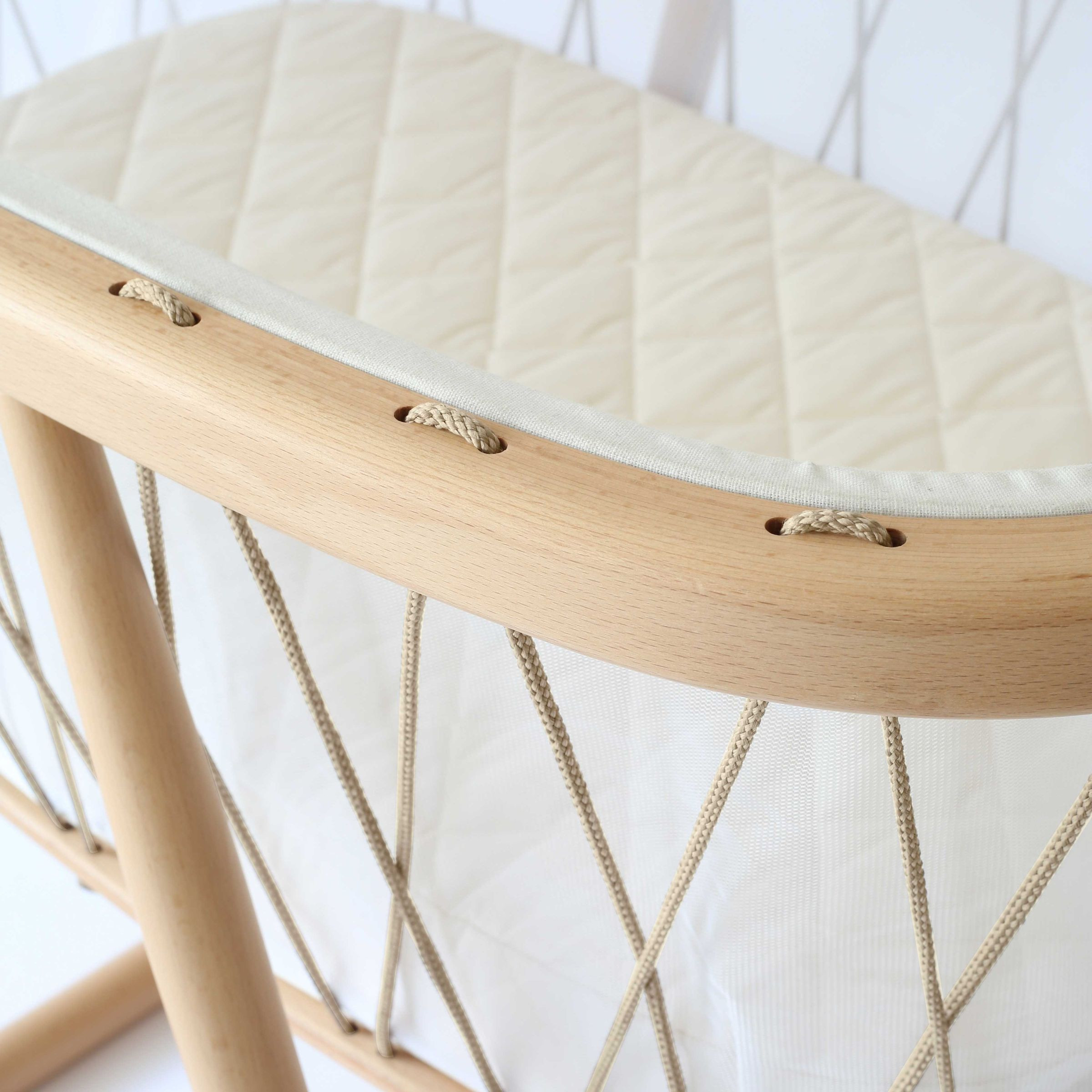 Close-up of the wooden frame and quilted seat of a bassinet.