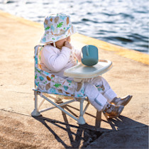 Child seated in booster chair by water with cup