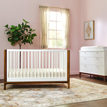 Crib in a pastel room with window and dresser visible